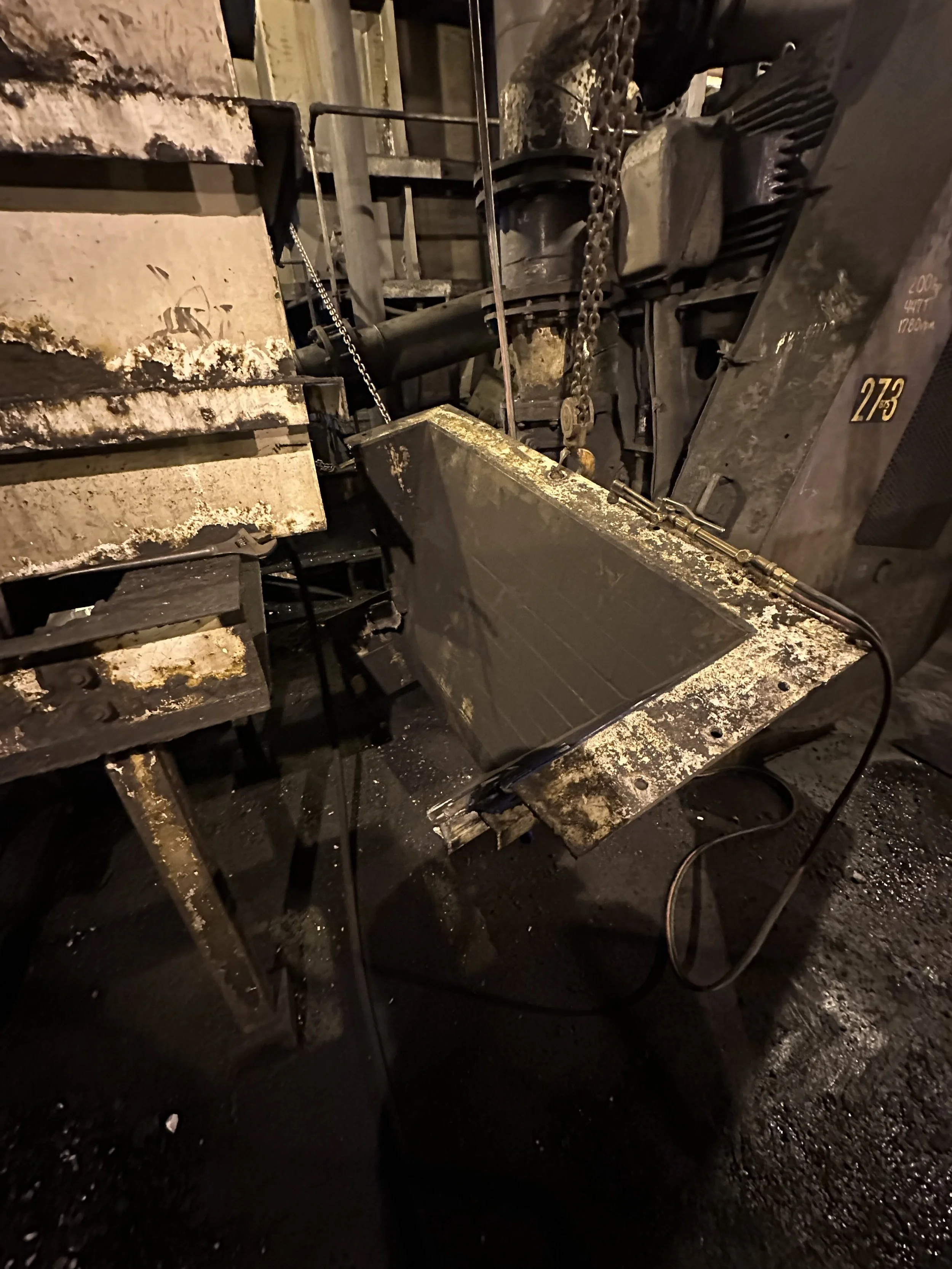 Close-up of a mechanical work area with metal tools and equipment, including chains and a metal work surface, in a dark setting.