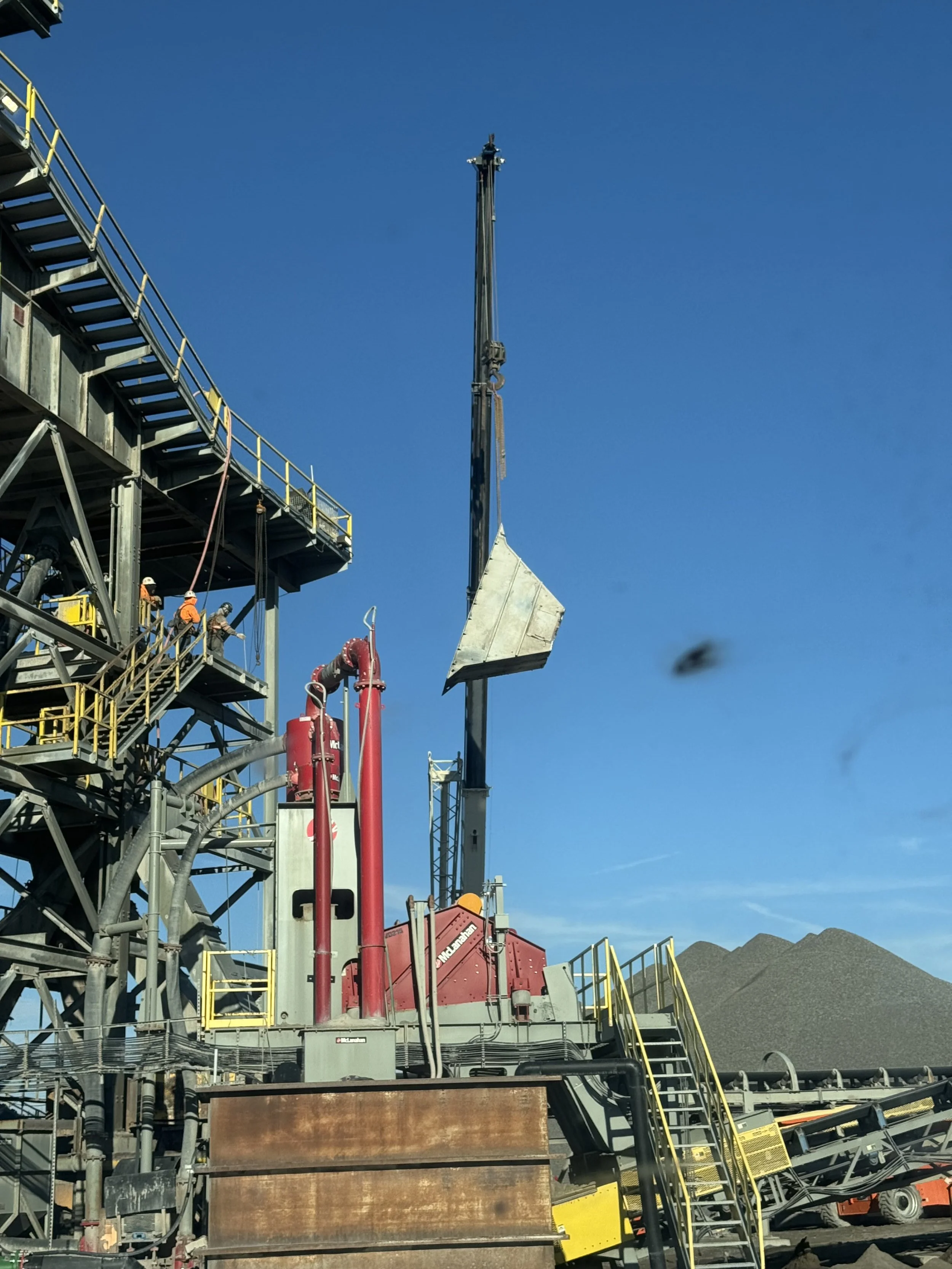 Construction workers operating machinery on a construction site against a clear blue sky.