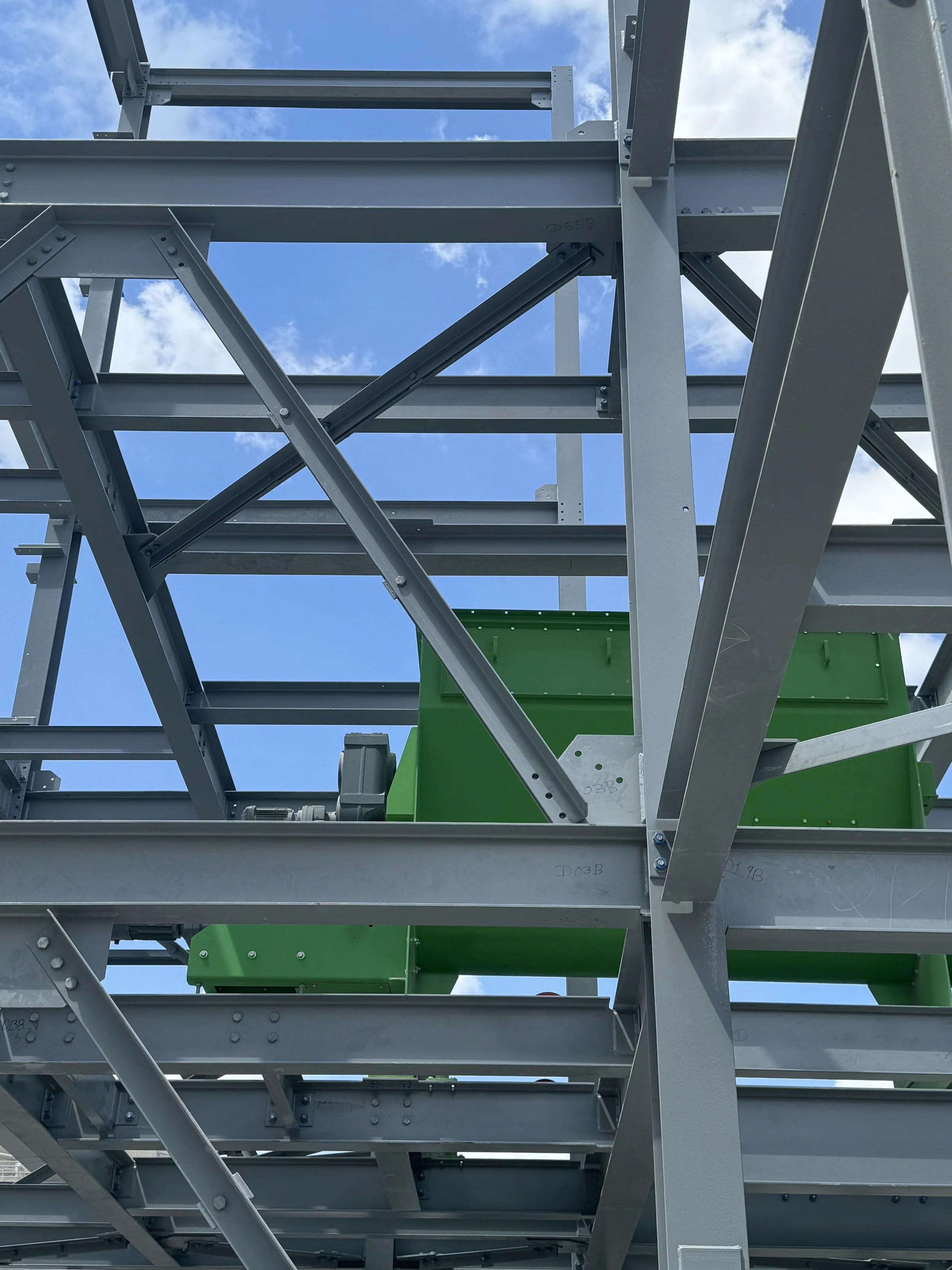 Steel framework structure under construction with a blue sky and clouds in the background.