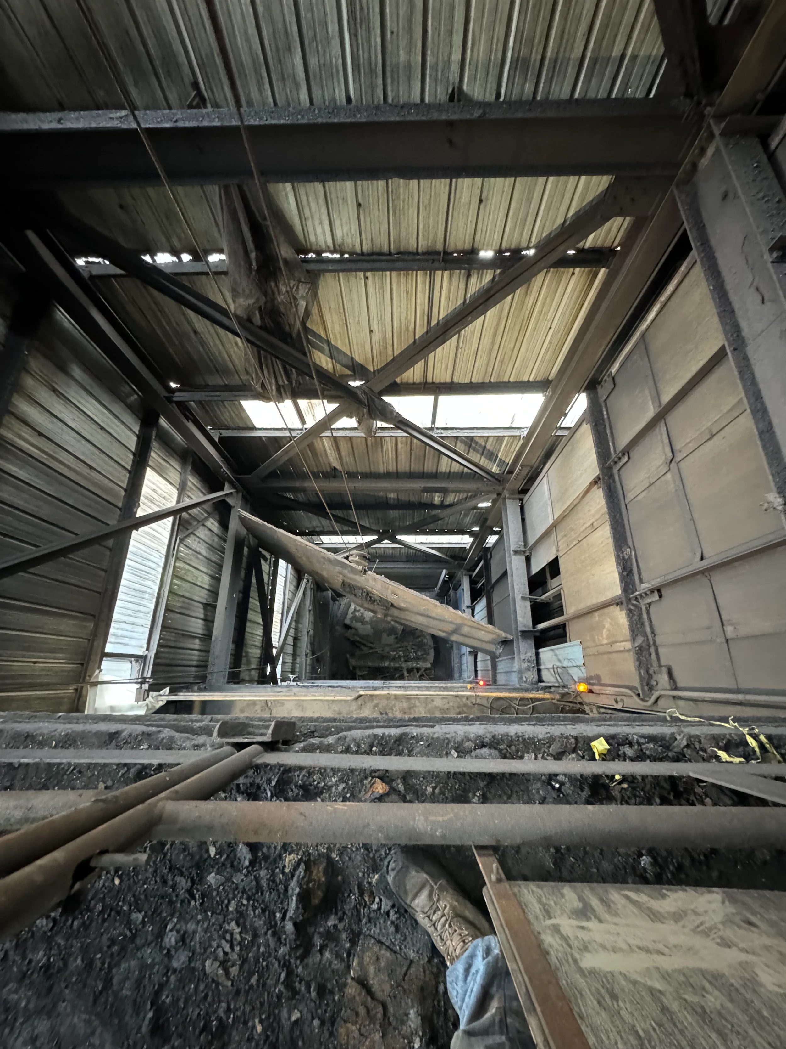Interior of a building under construction or repair, with visible wooden and metal framework, dirt, and construction tools and materials on the ground.
