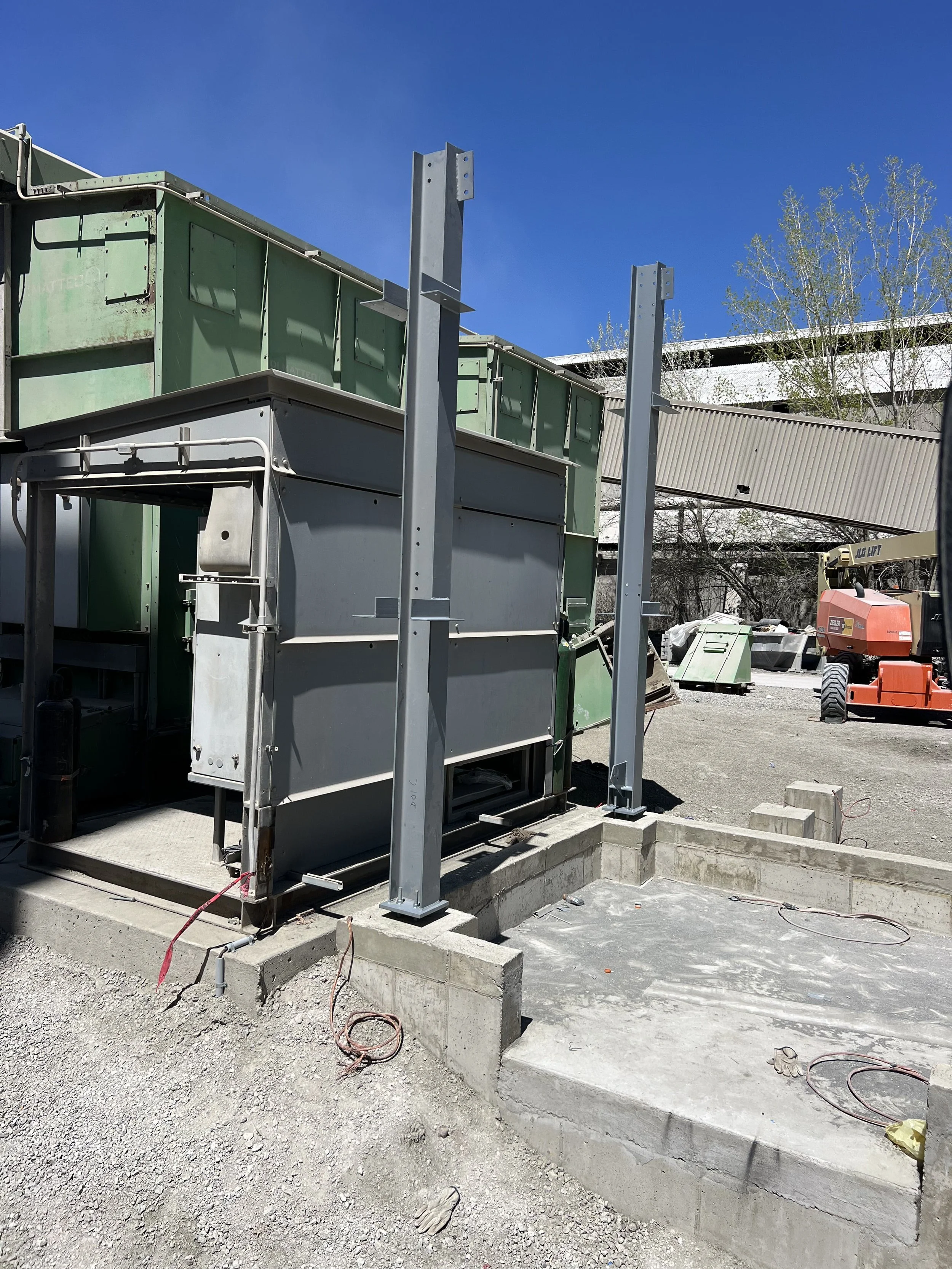 Construction site with concrete foundation, metal support beams, green electrical boxes, and construction equipment under a clear blue sky.