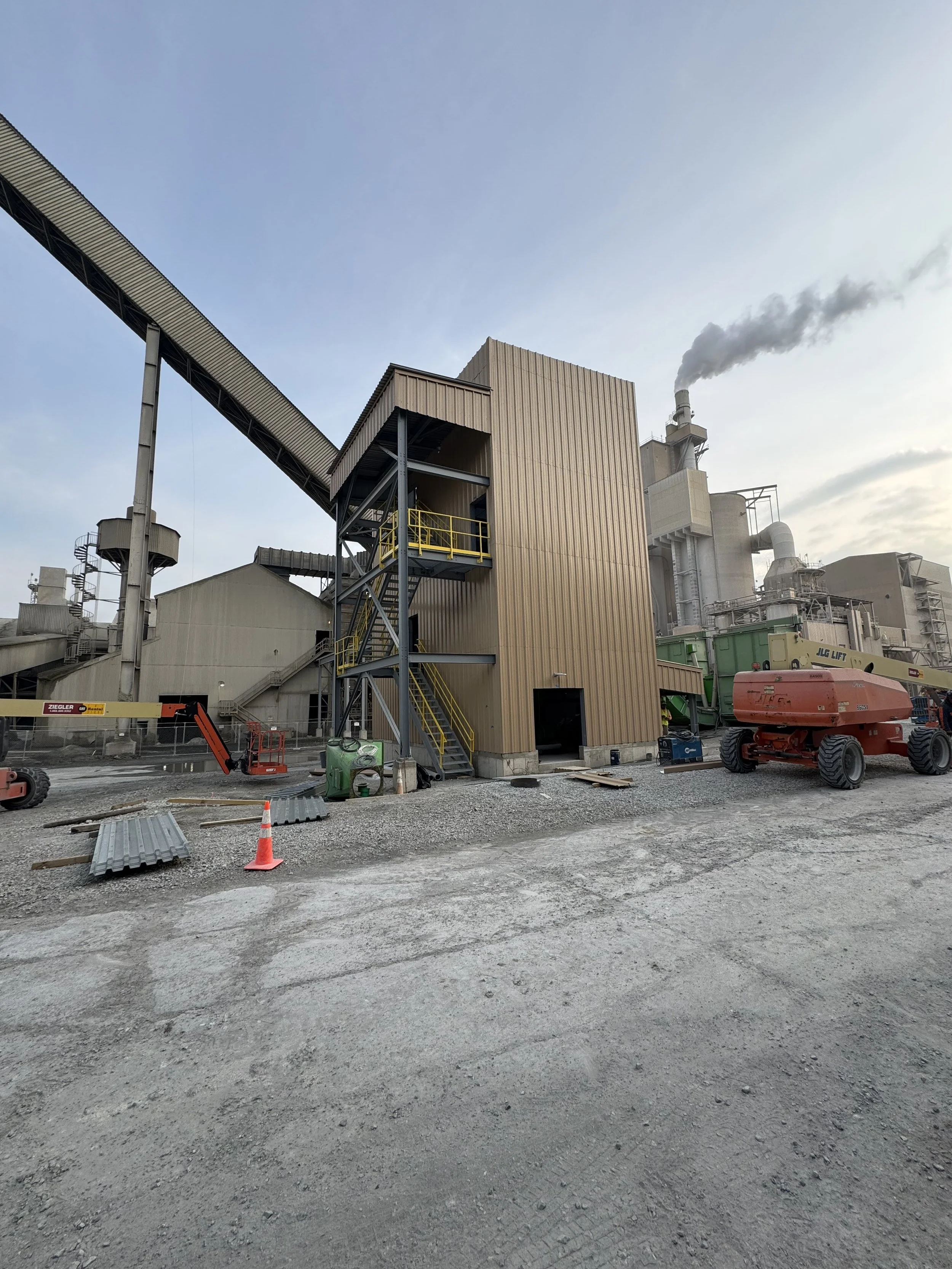 Construction site with industrial buildings, machinery, and a clear sky.