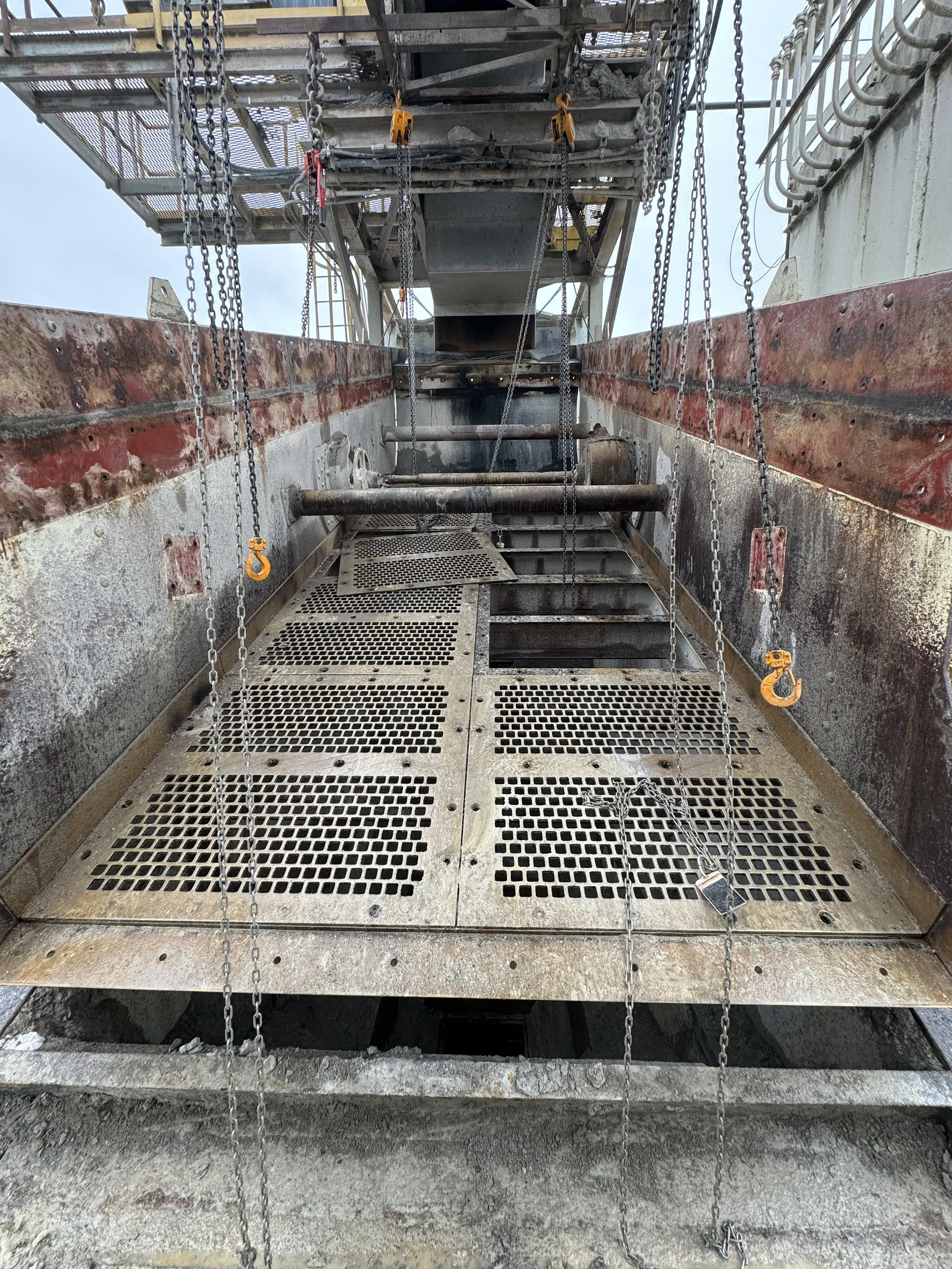 View looking up at a construction site with metal scaffolding, chains hanging, and metal grates for flooring, showing an unfinished building structure.