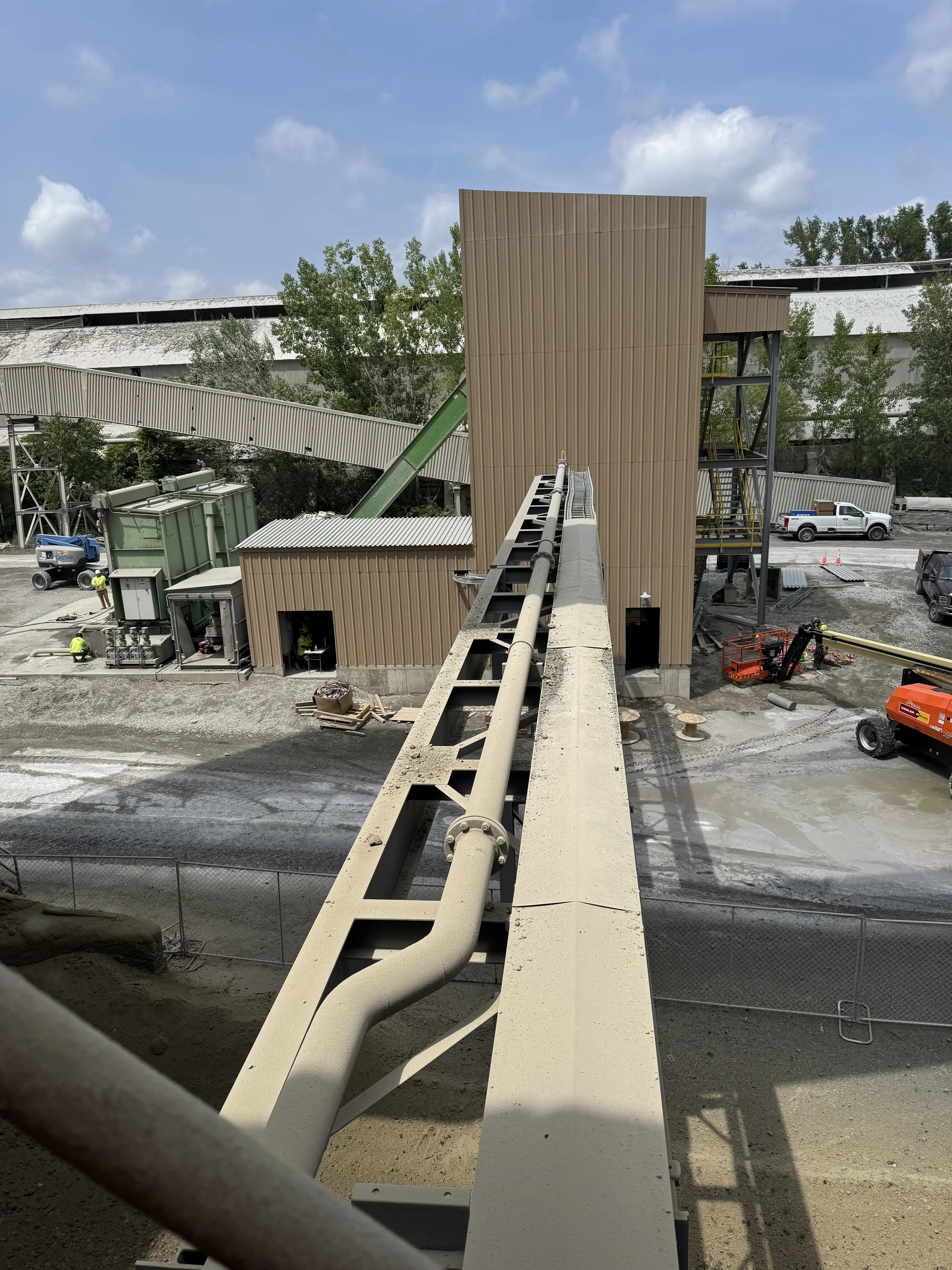 Construction site with a view from a bridge, showing a building with wooden siding, scaffolding, and construction workers.