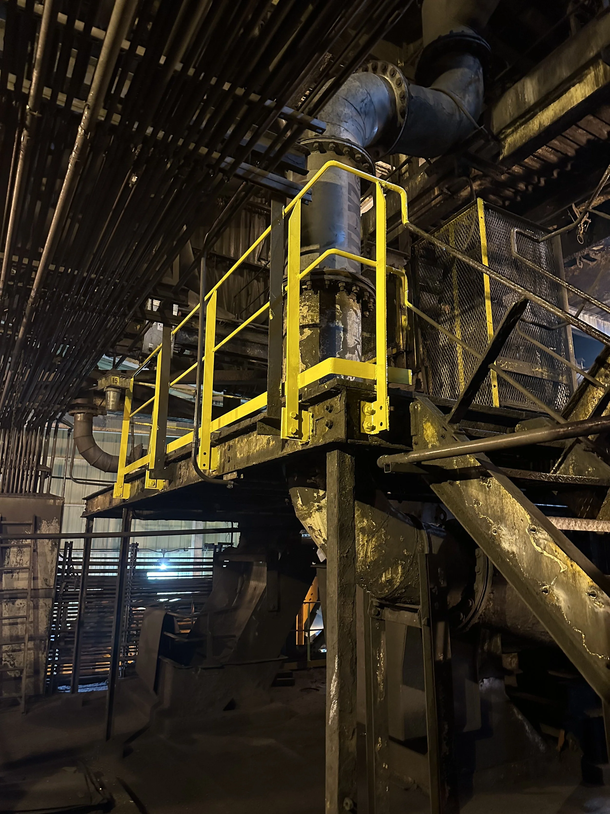 Industrial tunnel or piping system with large metal pipes and yellow safety railings.