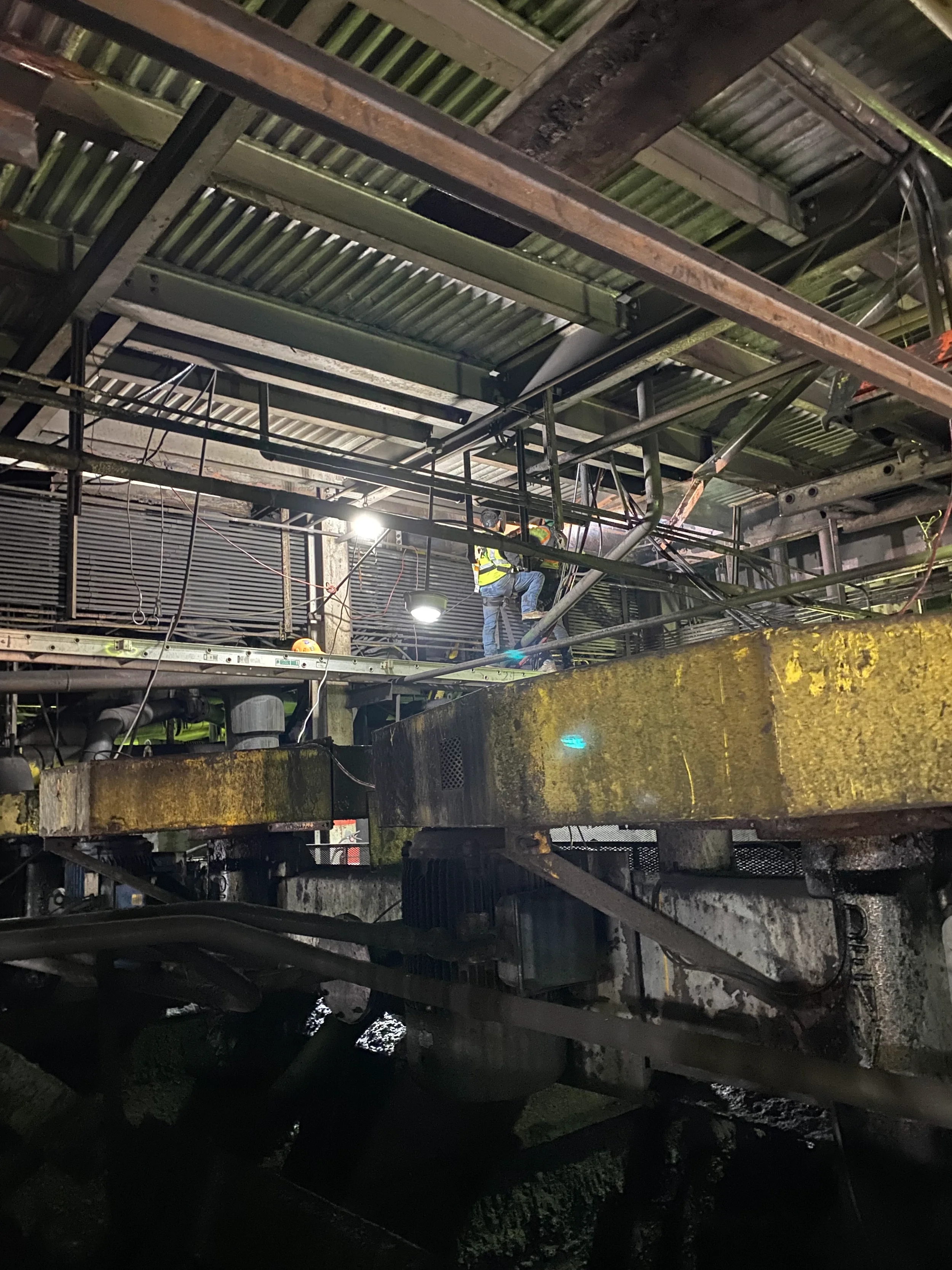 Construction workers working on scaffolding and framework inside an industrial or construction site during nighttime, with visible pipes, metal beams, and scaffolding.