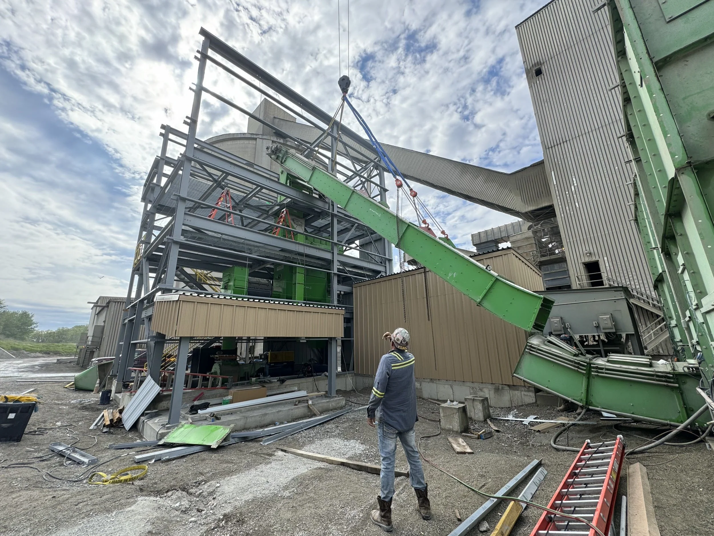 Construction workers inspecting a structure with a green slide or chute at an active construction site.