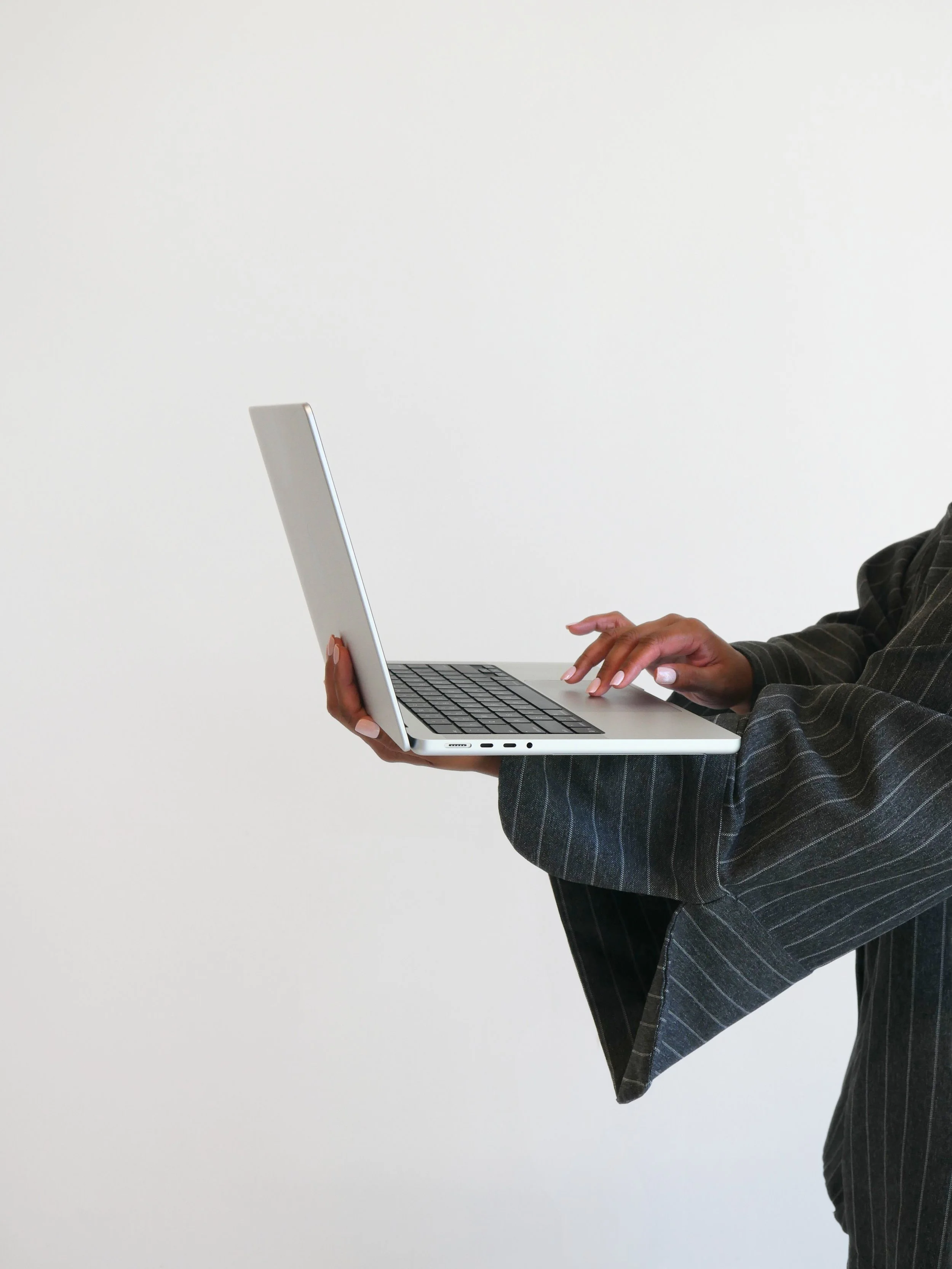 Person wearing a striped suit holding a silver laptop in front of a plain white wall.
