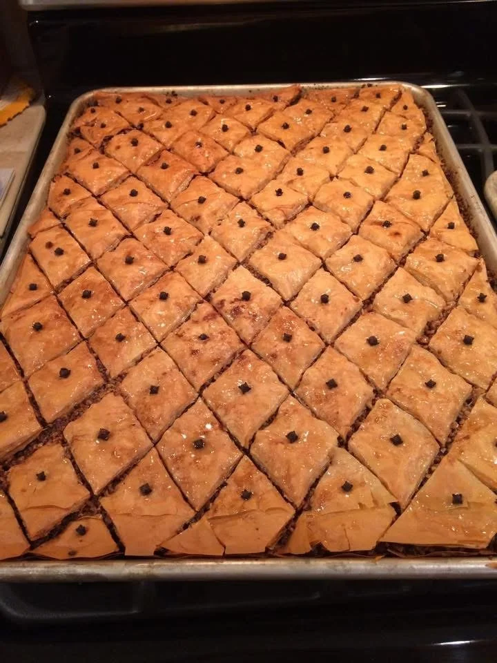 Tray of freshly baked baklava cut into diamonds, topped with a single clove on each piece.