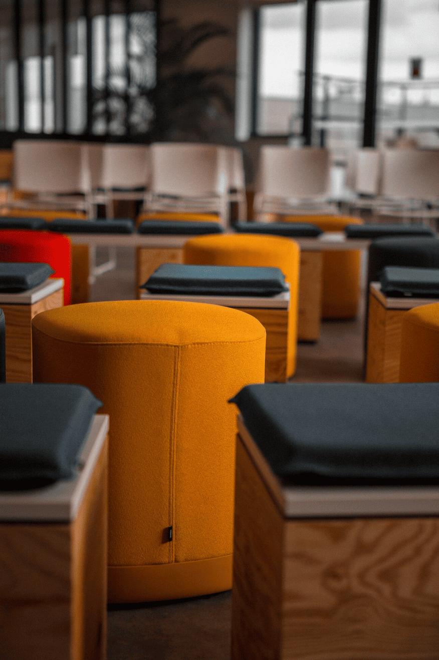 Empty chairs and ottomans in a modern, well-lit conference or lounge area with large windows.