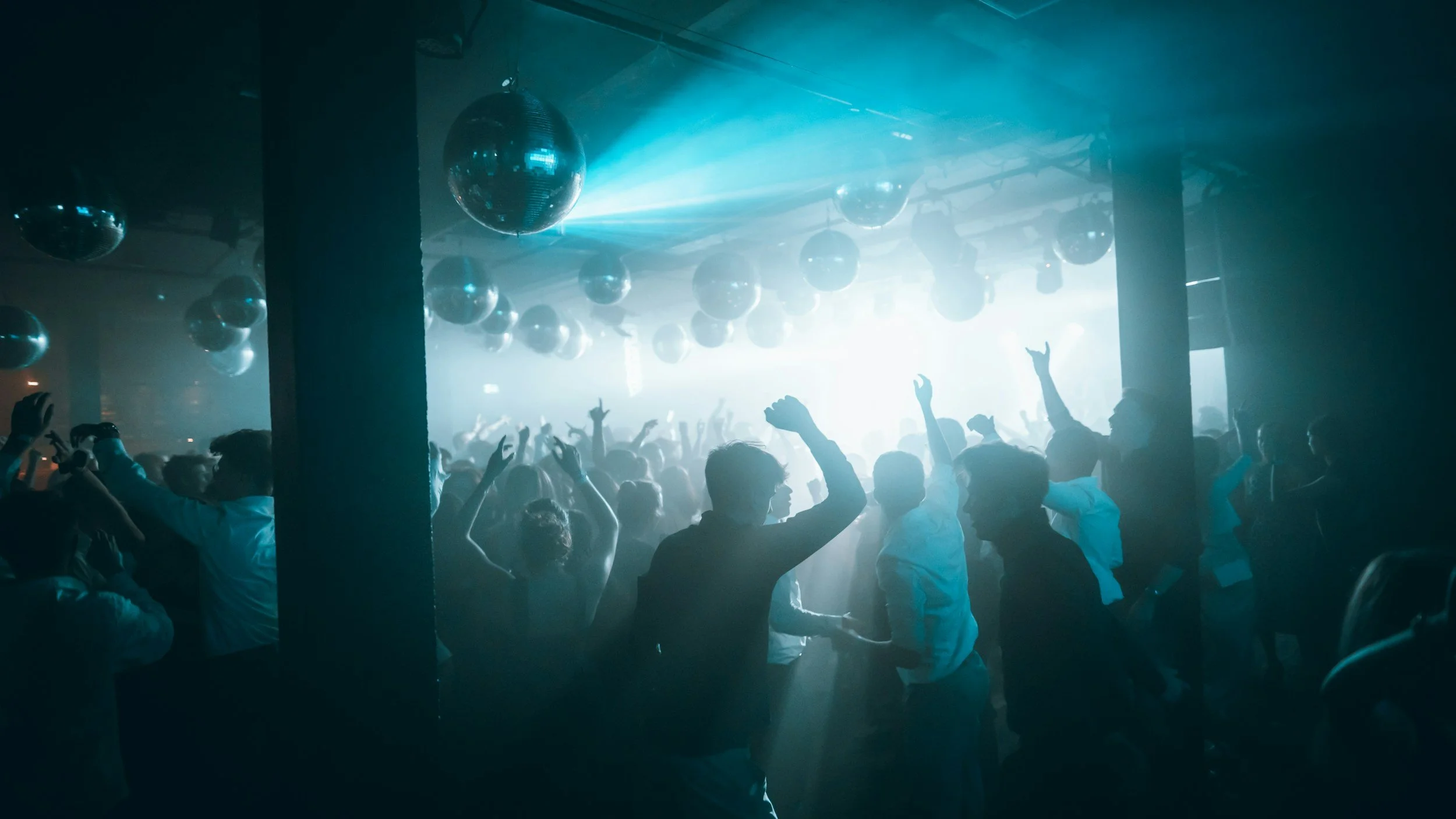 People dancing and celebrating in a dark venue with disco balls and bright blue lighting.