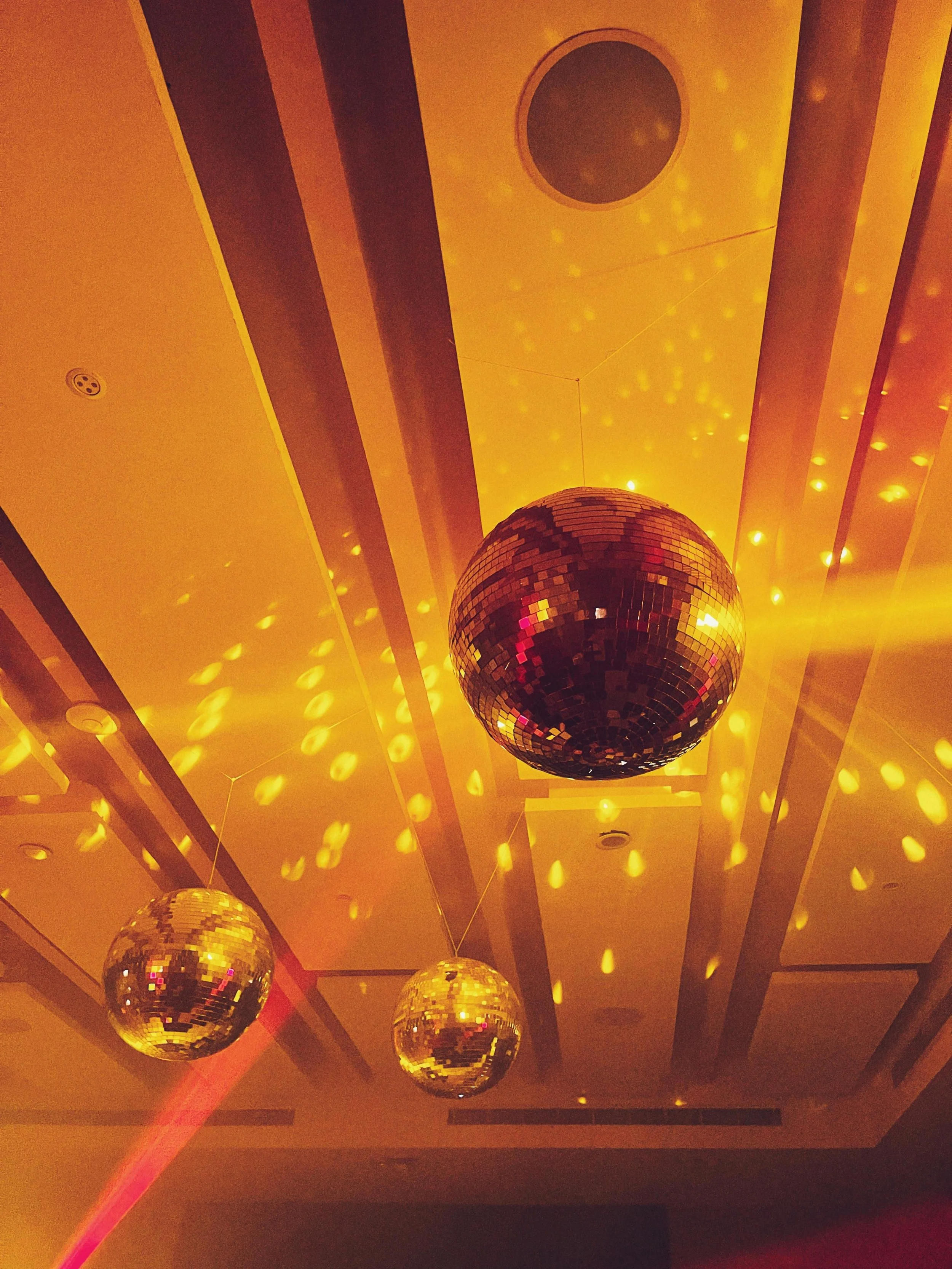 Ceiling with four disco balls hanging and lights creating yellow reflections on the ceiling.