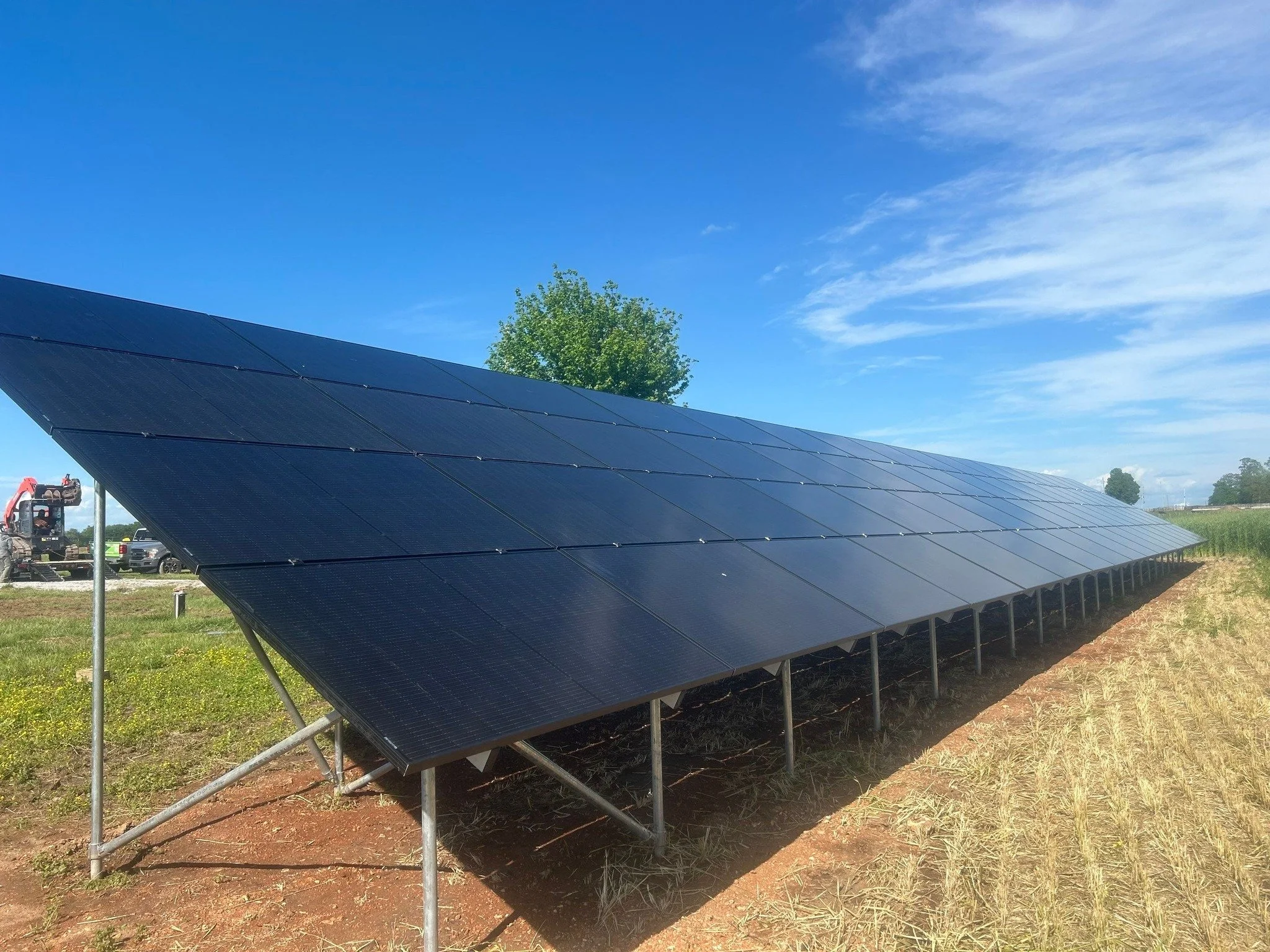 Solar panels installed on a grassy field with a clear blue sky and some clouds in the background.