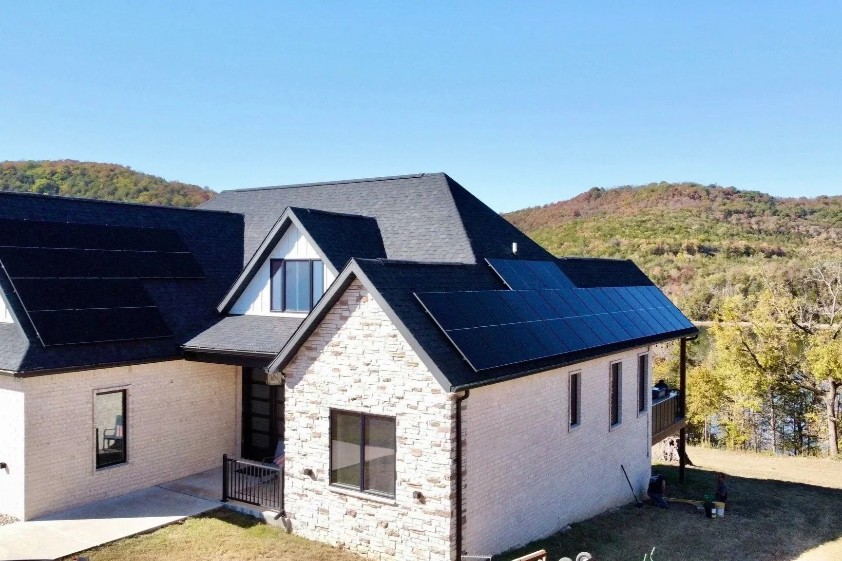 A modern house with solar panels on the roof, set against a backdrop of hills and trees.