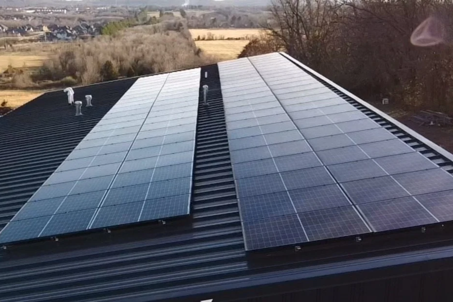 Solar panels installed on a black metal roof of a building in a rural area.