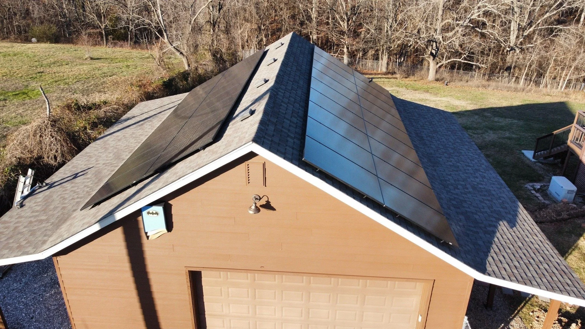 A residential house with solar panels installed on the roof, situated in a yard with trees and grass.