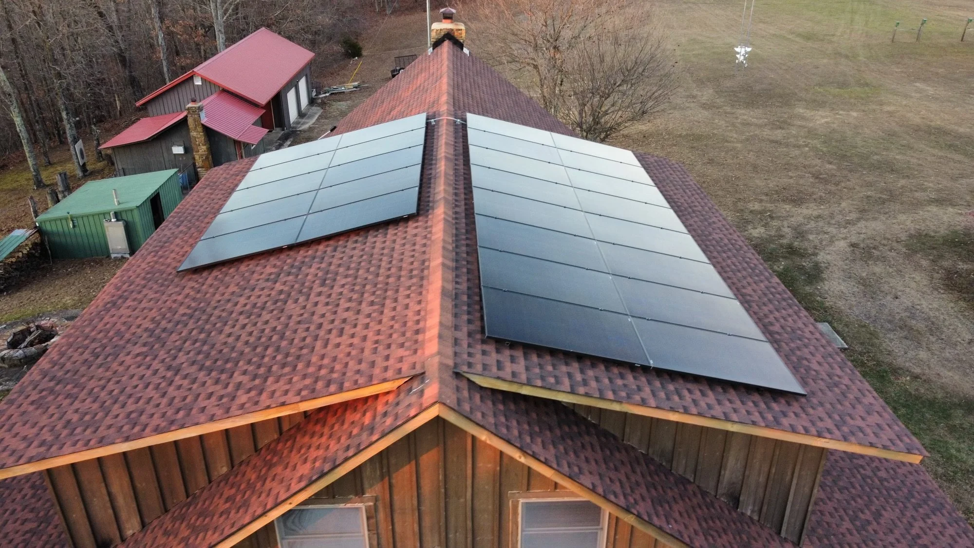 A house with solar panels installed on its red tile roof in a rural area with trees and open land in the background.