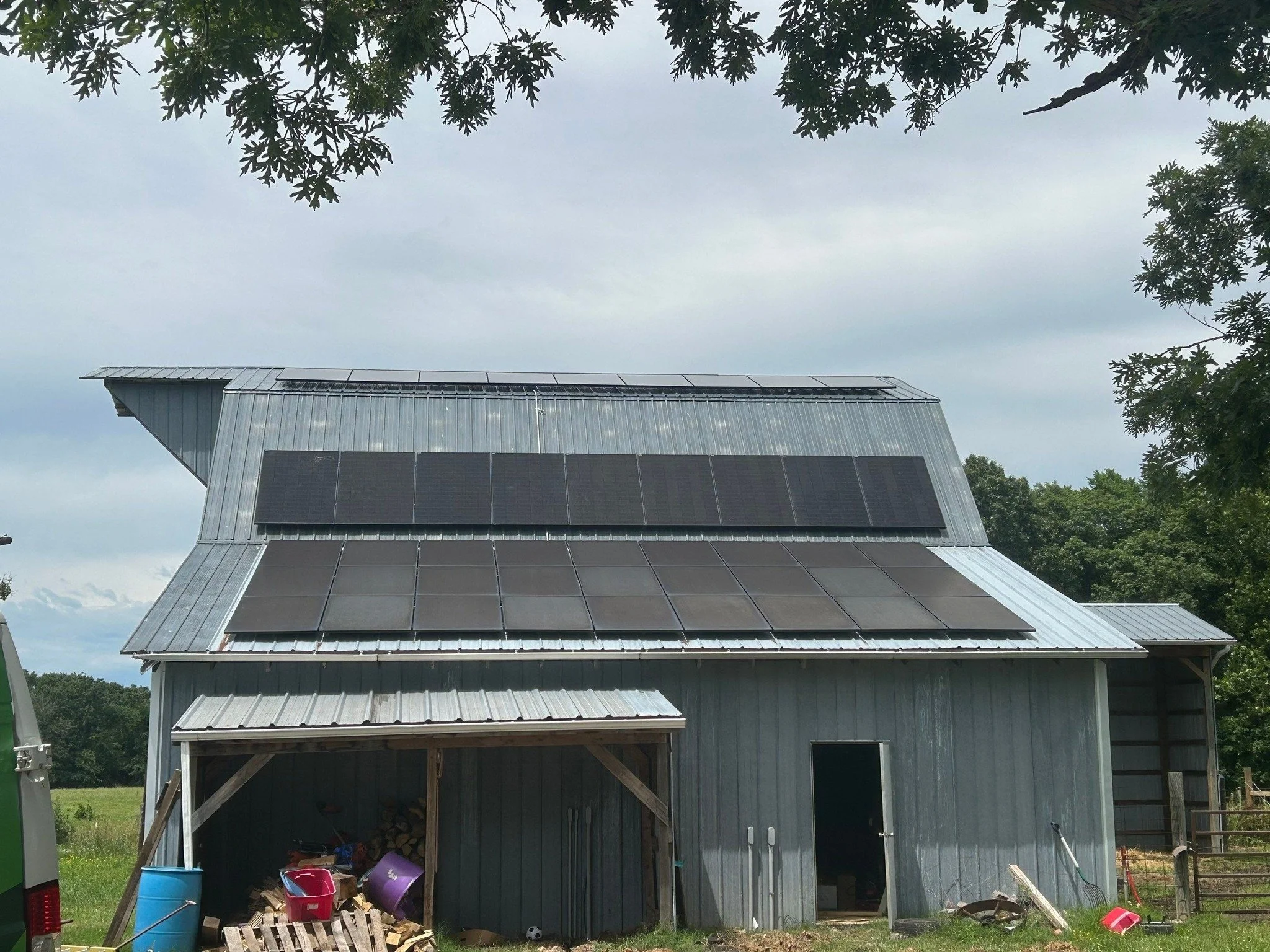 A grey metal barn with solar panels on its roof, surrounded by trees and outdoor toys lying on the ground.