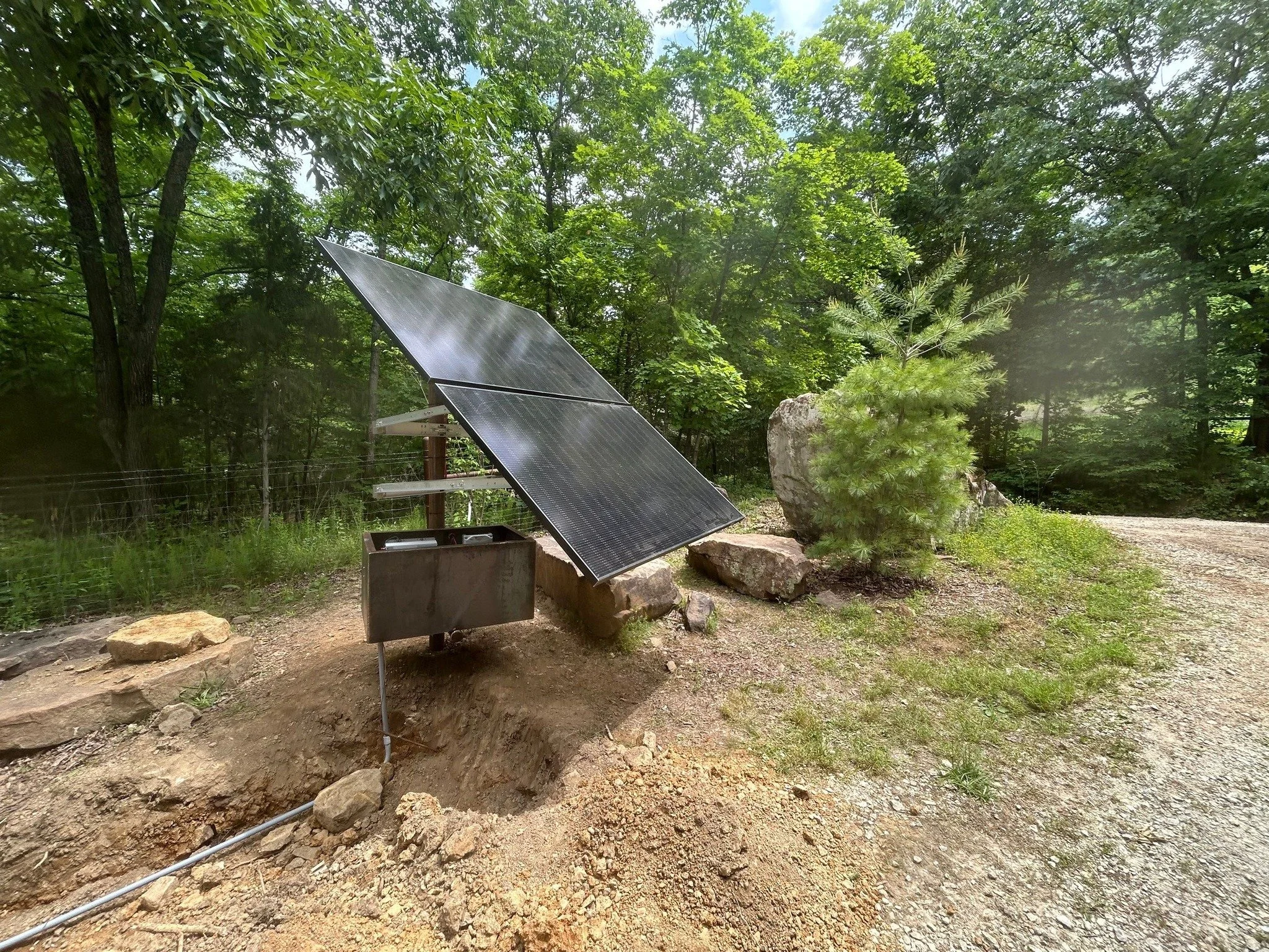 Solar panel installed on the ground near rocks and trees in a wooded outdoor area.