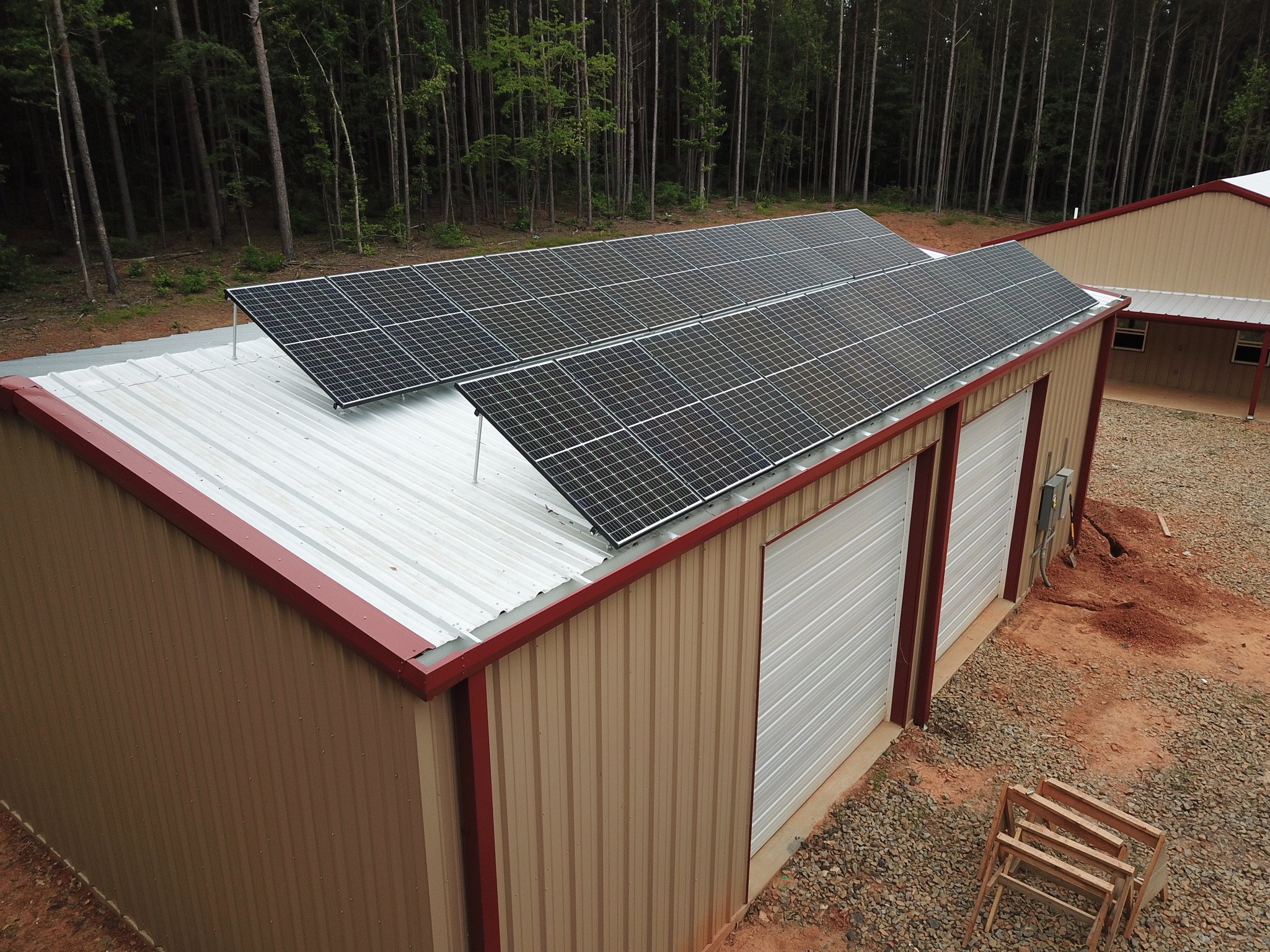 View of solar panels installed on the roof of a building in a forested area, with trees in the background and construction materials nearby.