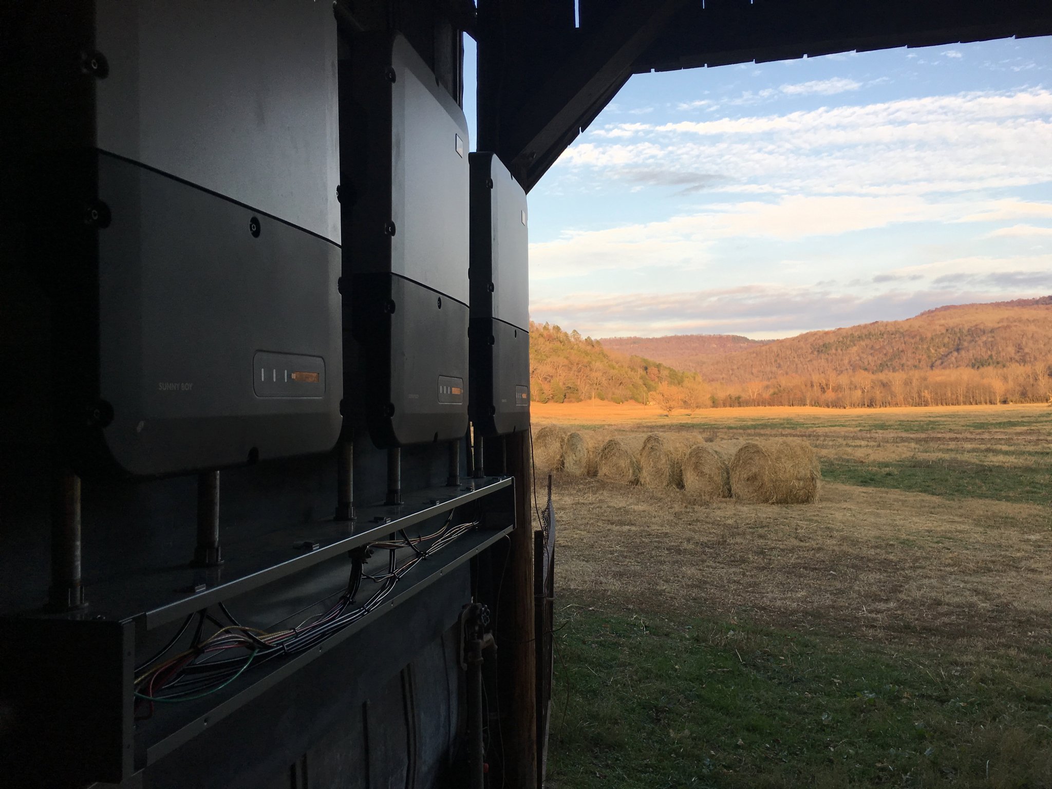 Field with hay bales and hills in the distance, seen through the opening of an electrical box or machinery at sunset.