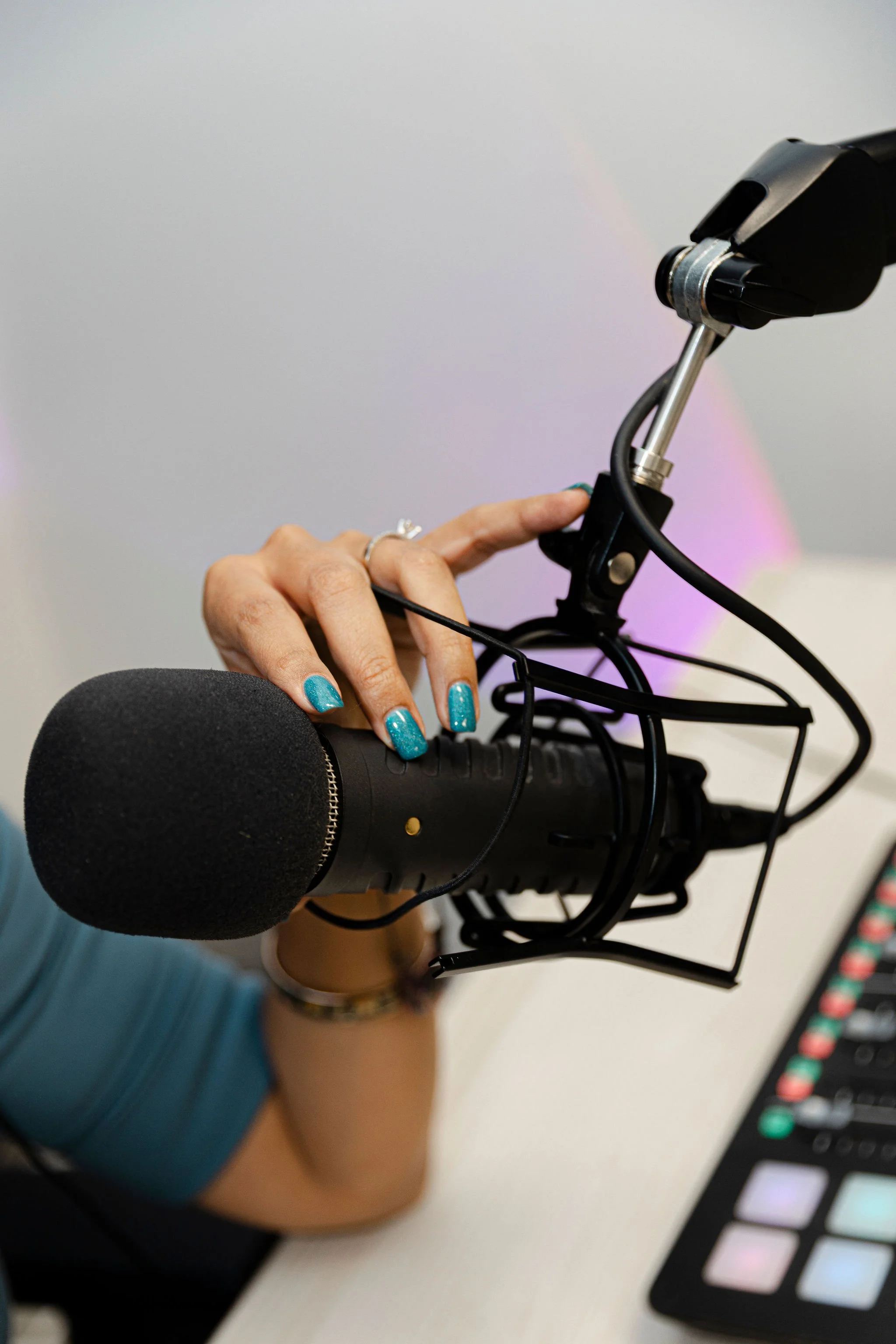 A person wearing teal clothing and teal nail polish holding a black microphone and adjusting the microphone's stand, with a digital audio workstation interface visible in the bottom right corner.