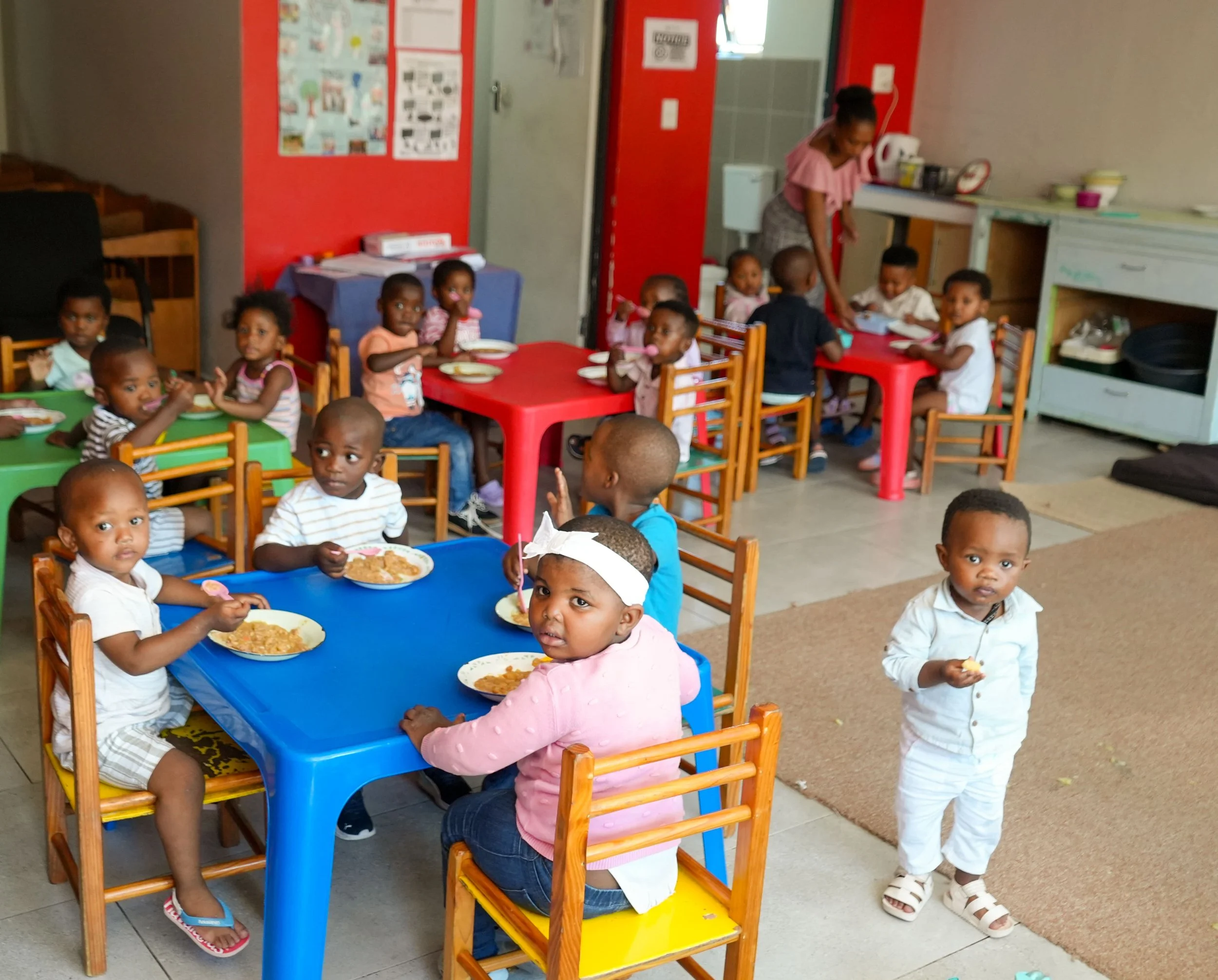 Kleinkinder von Baphumelele essen an ihren kleinen Plastiktischen zusammen zu Mittag.