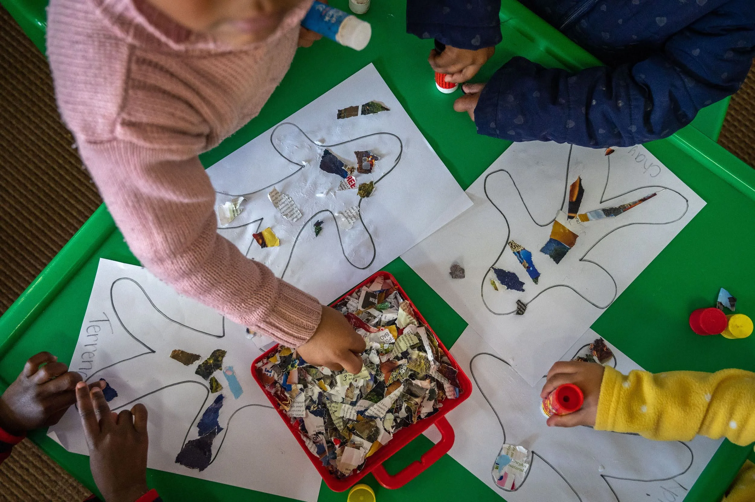 Kindern basteln mit Papierstückchen und Leimstiften Menschen.