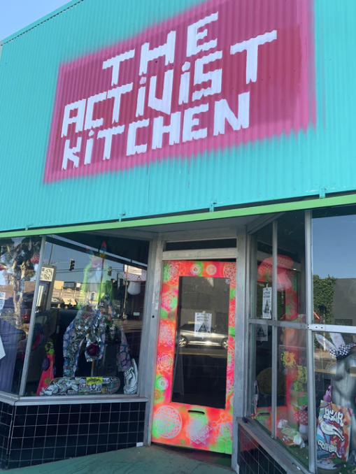 Sign that reads 'The Abstract Kitchen' above the entrance of a colorful storefront with large windows showcasing clothing and decorations
