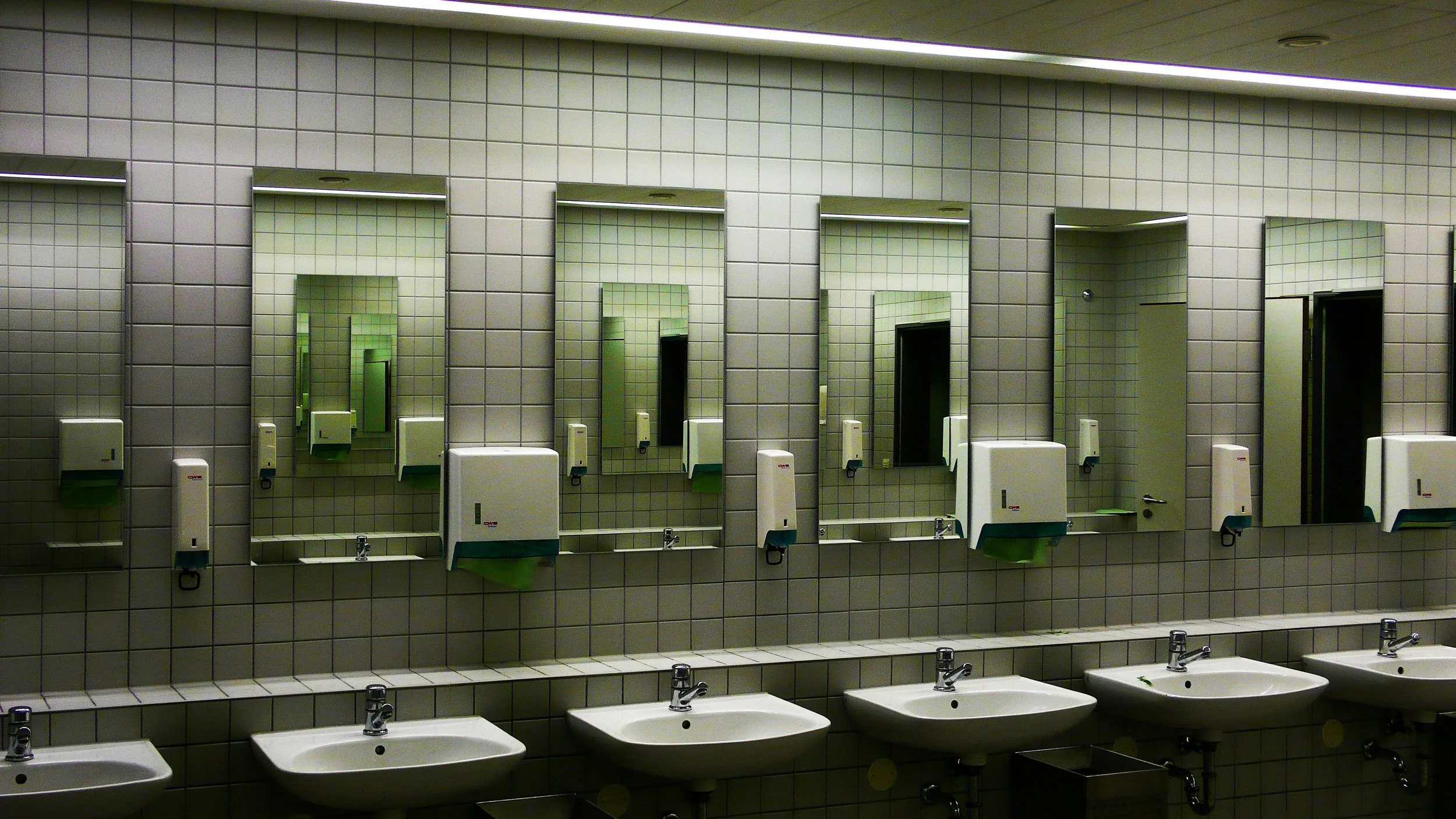 Multiple white sinks and sinks with mirrors and soap dispensers in a public restroom.
