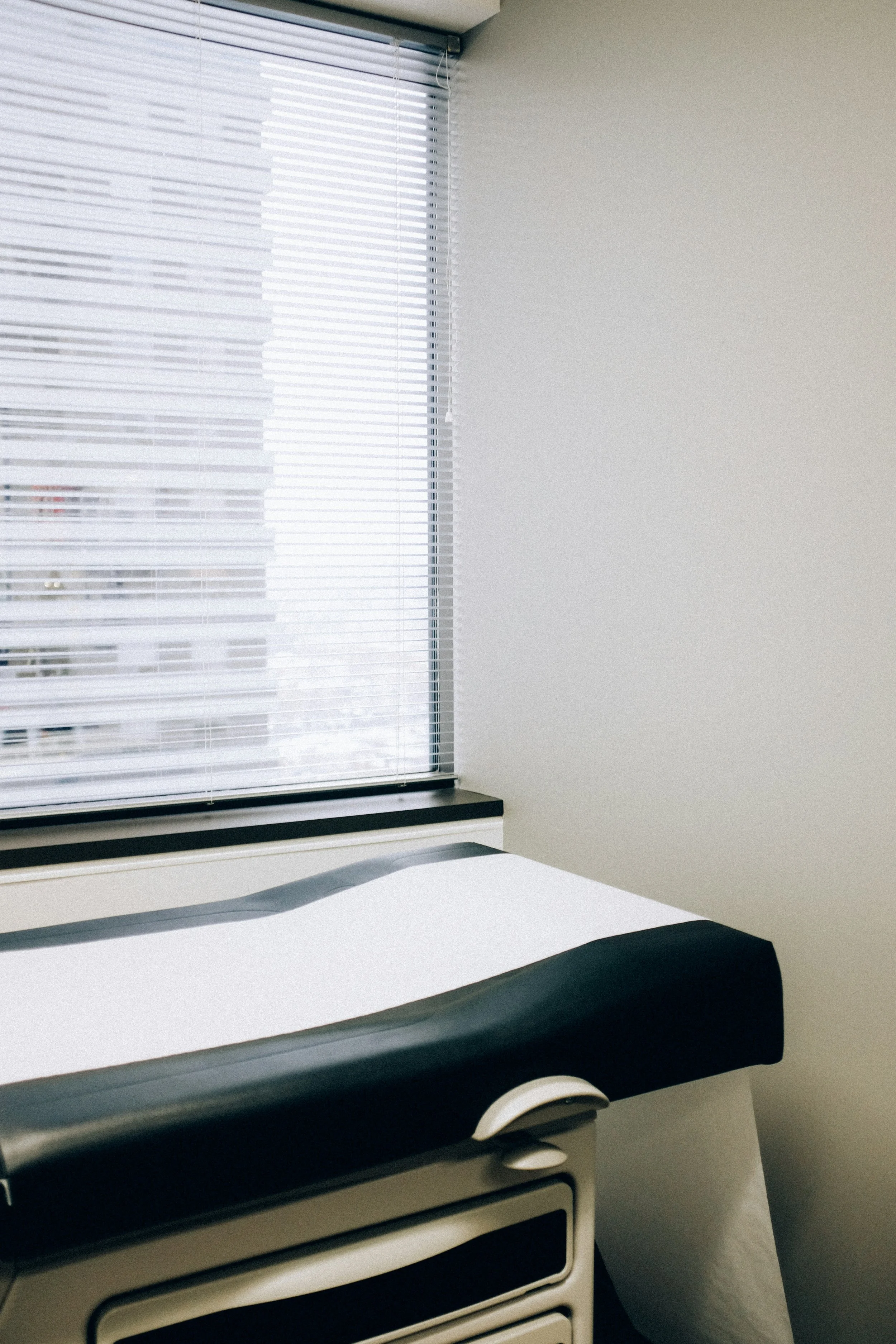 A room with a window with closed blinds, a white table, and a black office chair.
