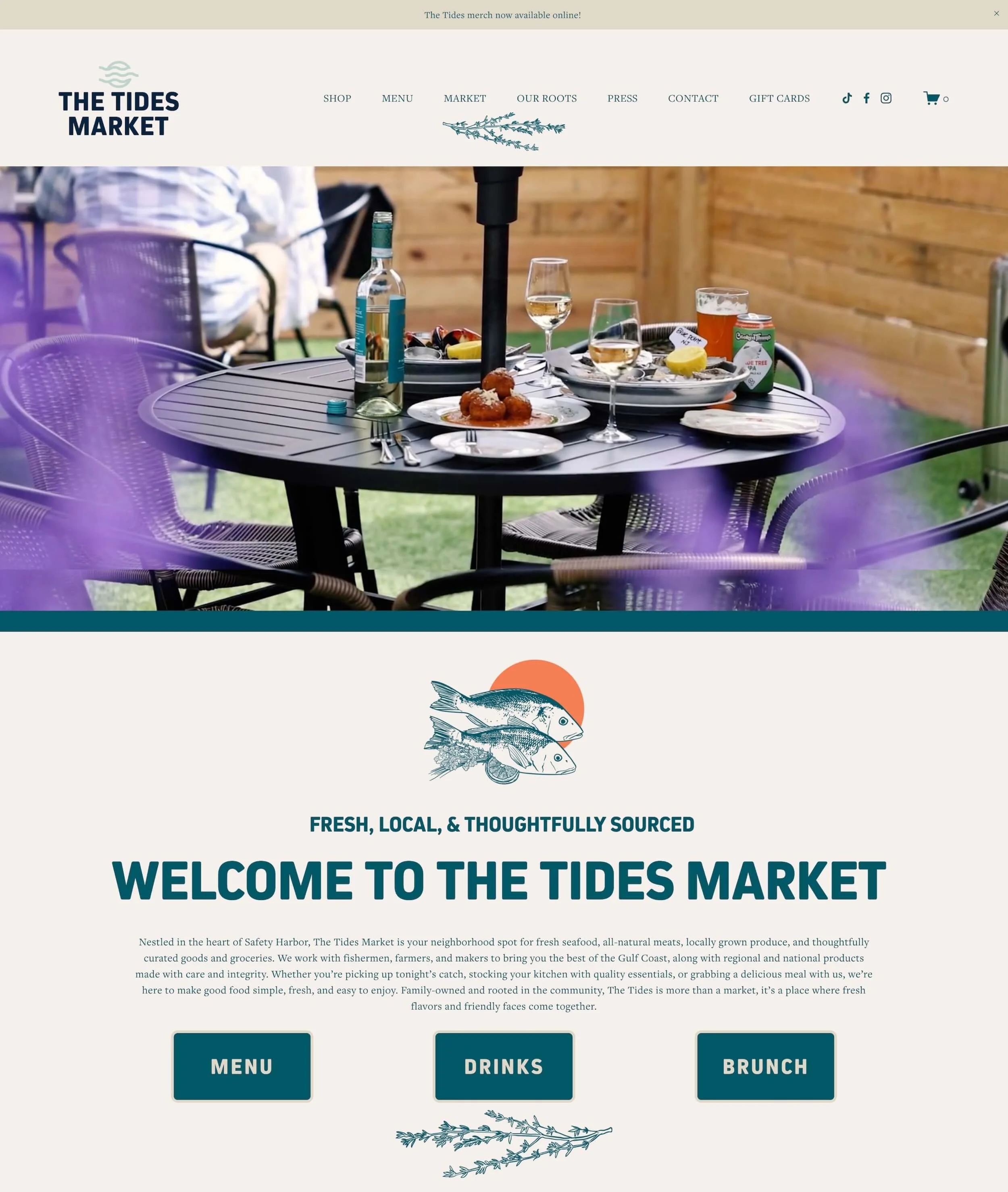 Screenshot of The Tides Market website homepage featuring a welcoming message, navigation menu, and a photo of a table set with food and drinks outside, with a wooden fence in the background.