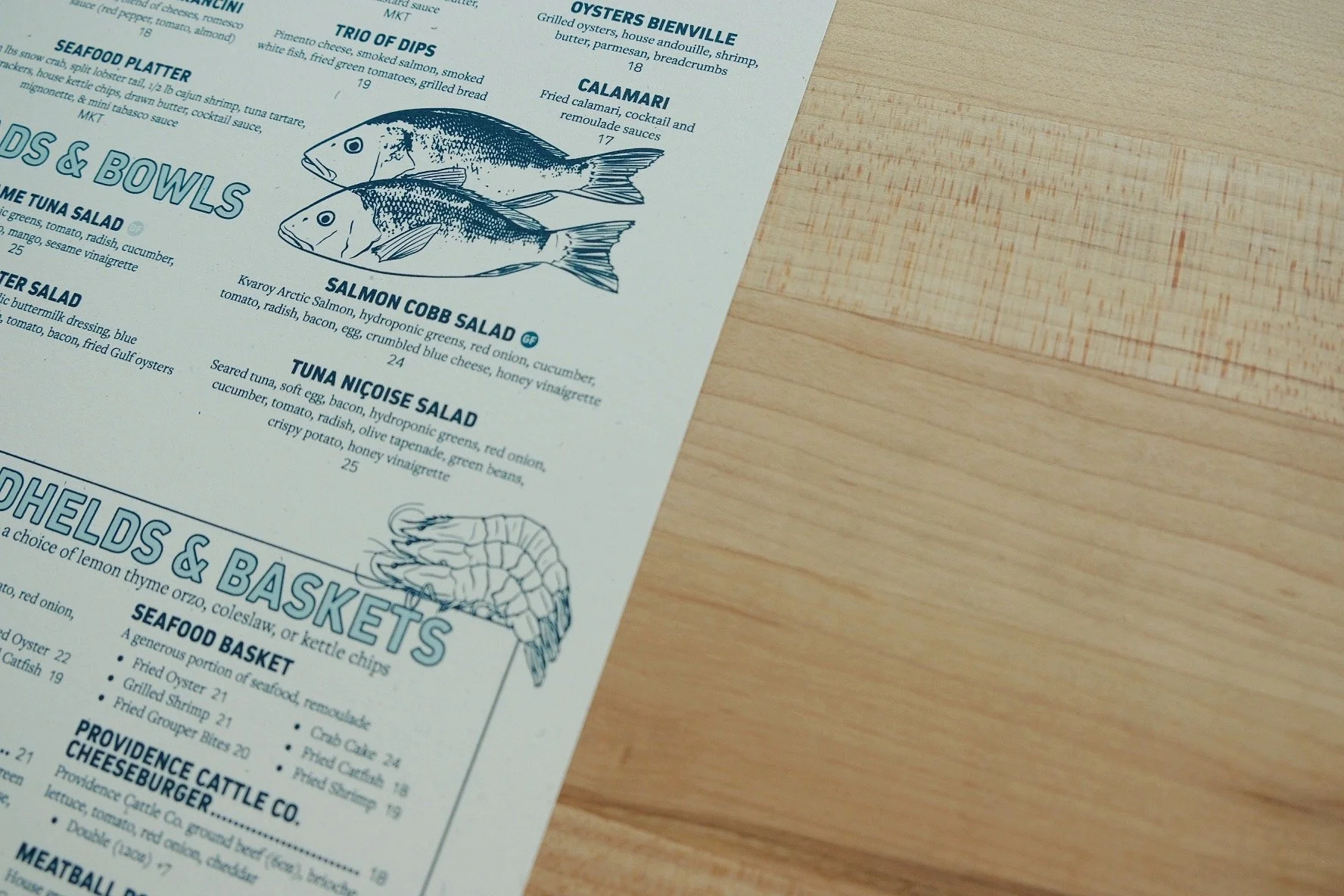 Part of a seafood restaurant menu with illustrations of two fish, and a shrimp, including prices and descriptions.