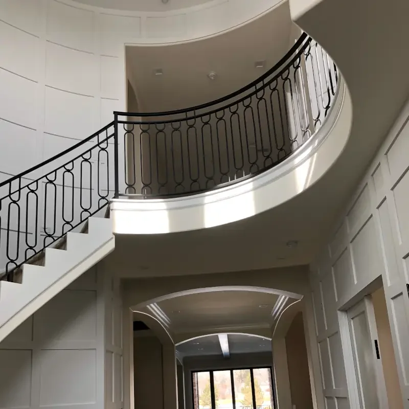 Luxury interior painting and fine finish project featuring a curved staircase, custom wall panel molding, black iron railings, and elegant architectural detailing in a high-end custom home. Professional interior painting and custom finish services fo