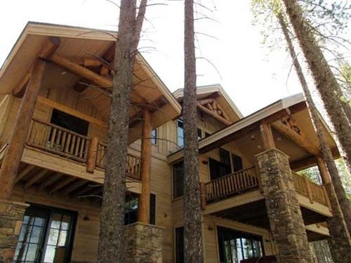 Luxury mountain-style residential exterior featuring natural wood siding, exposed timber framing, stone masonry accents, elevated decks, and custom architectural stain finishes. Professional exterior painting, wood staining, siding finishing, and mai