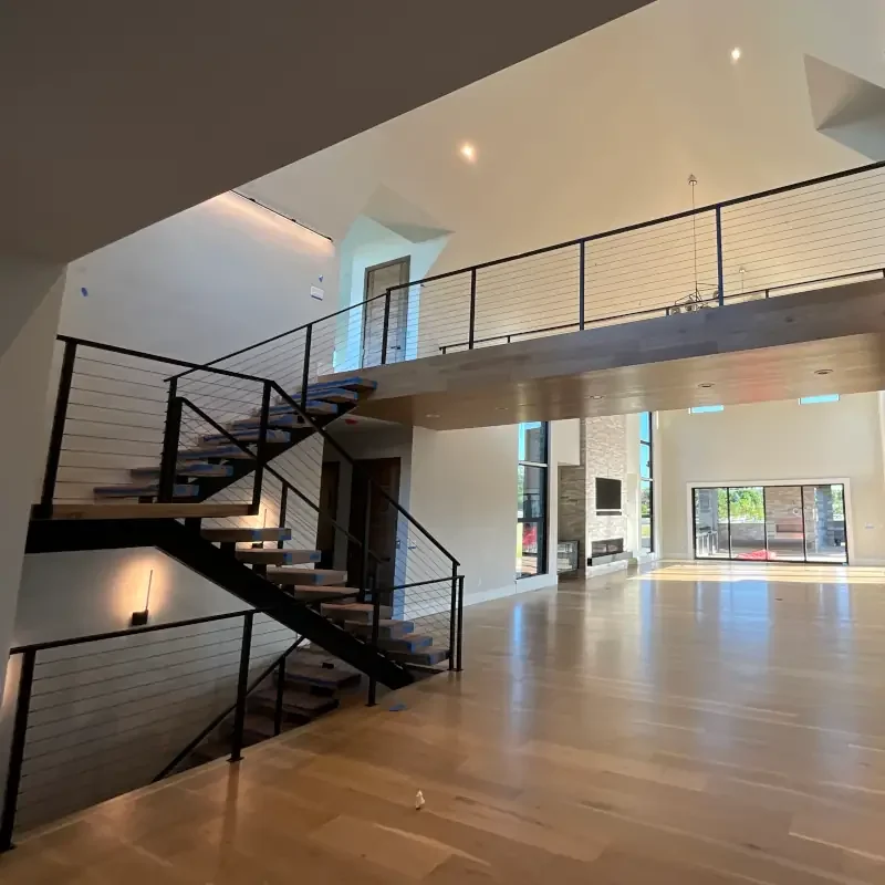 Modern interior painting and fine finish project featuring floating wood stair treads, black metal railings, vaulted ceilings, and expansive open-concept living spaces in a luxury custom home. Professional interior painting and custom finish services