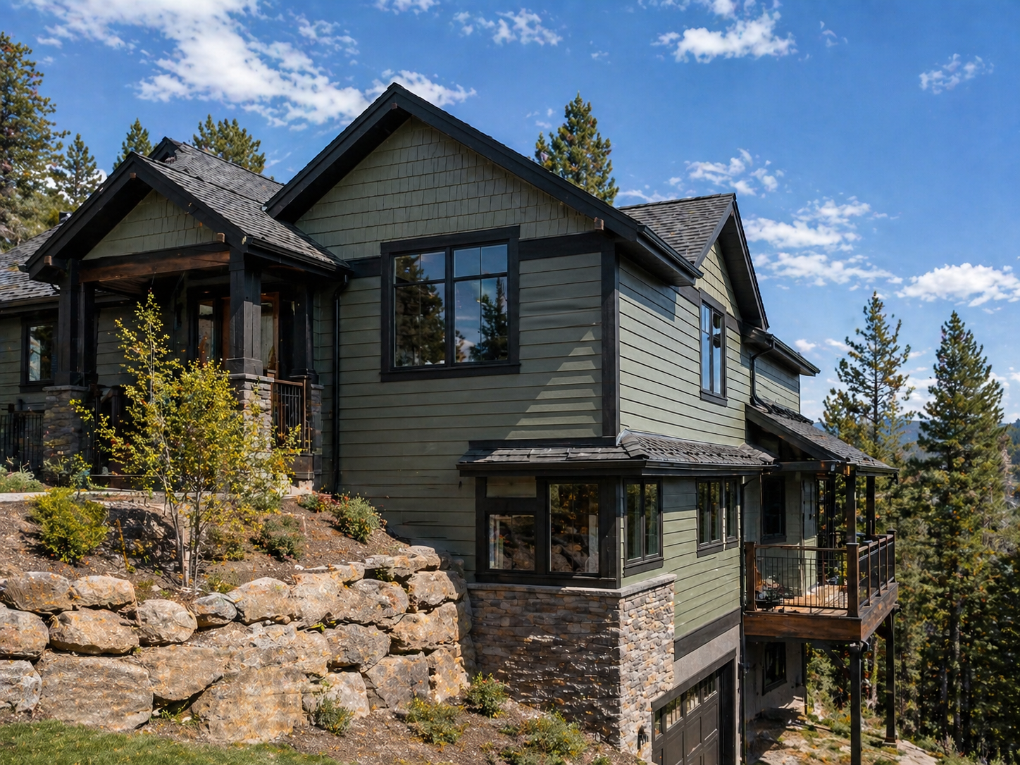 Multi-level residential mountain home on a steep hillside with painted exterior siding, elevated decks, retaining walls, and difficult-access exterior surfaces requiring specialized residential painting access.