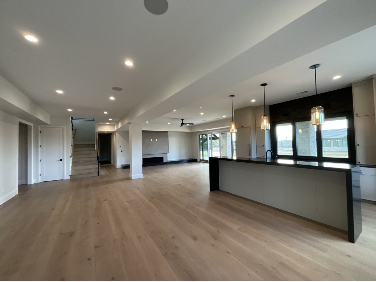 Modern open-concept interior painting project featuring custom cabinetry, luxury kitchen finishes, recessed lighting, wide plank hardwood flooring, and clean contemporary design. Professional interior painting and finishing services for custom homes,