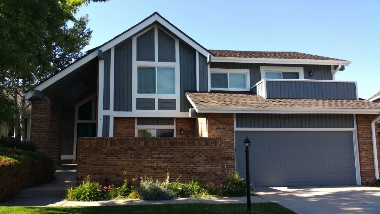 Freshly painted residential exterior with modern gray siding, white trim, brick accents, and updated curb appeal for Colorado suburban home.