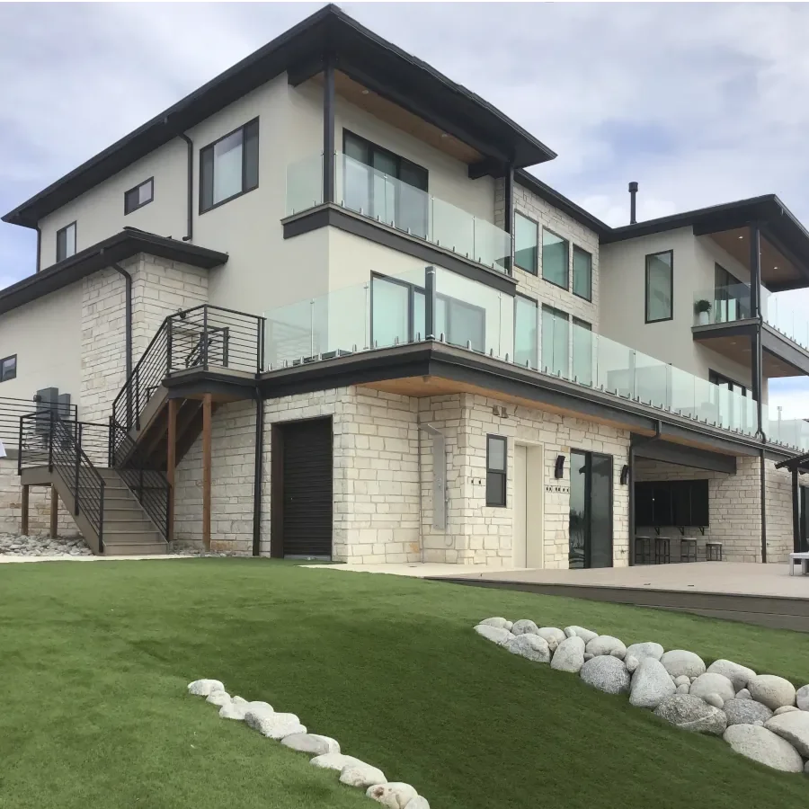 Modern luxury exterior painting project featuring smooth contemporary finishes, natural stone masonry, black trim accents, and expansive outdoor living spaces with custom glass railings. Professional exterior painting and finishing services for custo