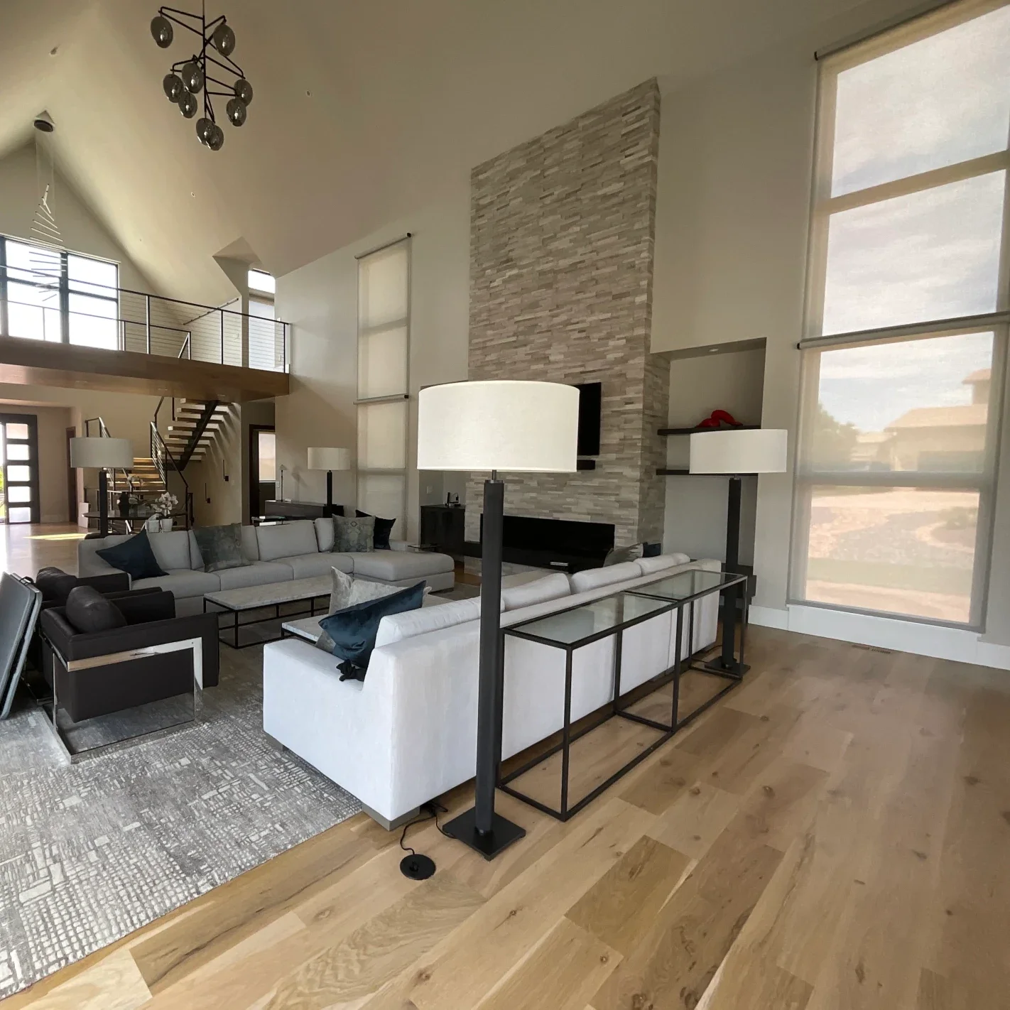 Luxury living room interior painting project featuring vaulted ceilings, oversized windows, modern black railings, custom stone fireplace detailing, and expansive open-concept architecture. Professional interior painting and fine finish services for 