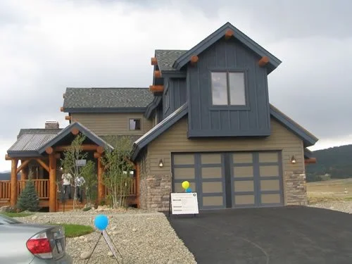 Exterior painting and staining project on a custom mountain home featuring bold dark siding, natural timber accents, stonework details, and rustic modern architectural finishes. Professional residential painting services for custom homes, mountain pr