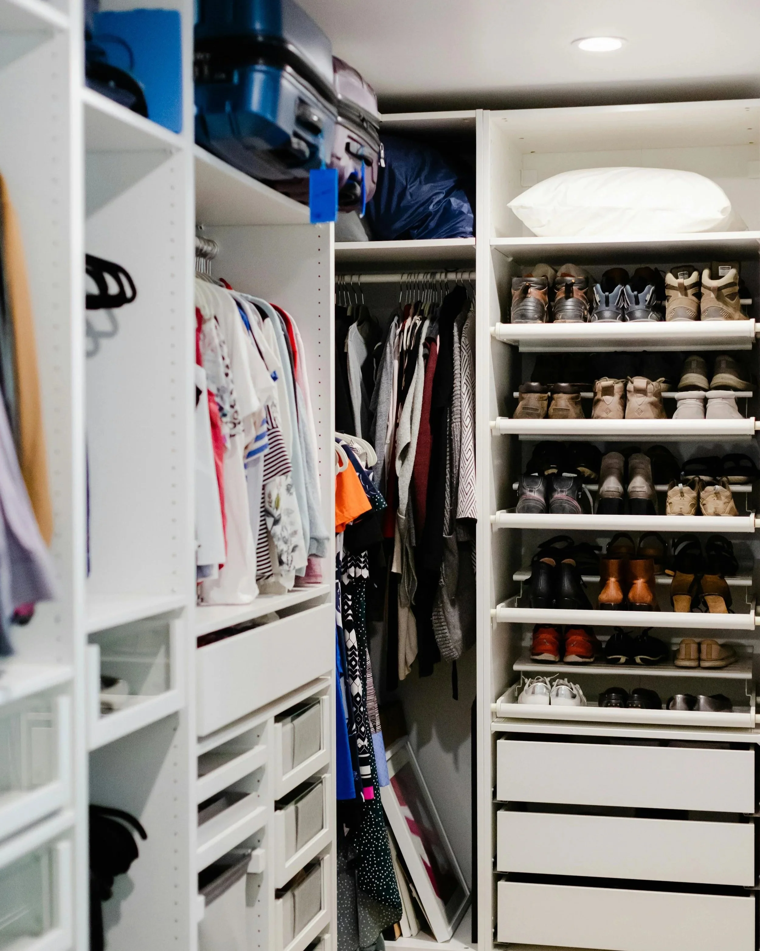 A walk-in closet with clothes, shoes, and storage boxes organized on shelves and racks.