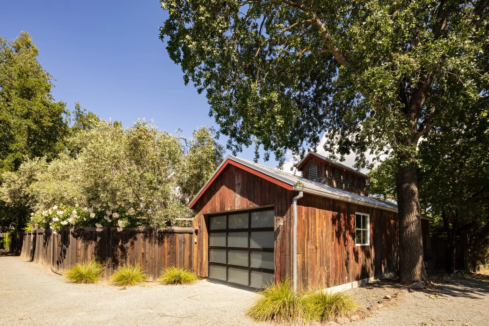 A small wooden house with a large window, set against trees and a clear blue sky.