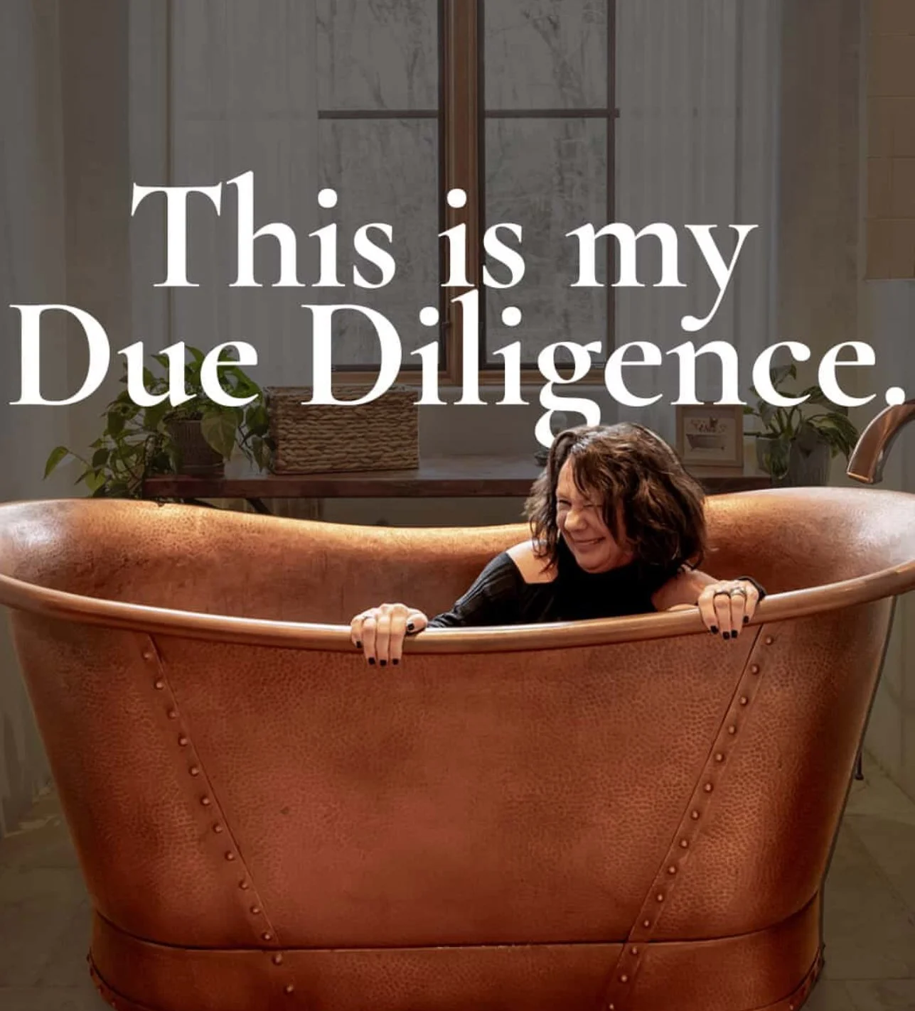 Shayne Hollifield is smiling and leaning out of a large, copper-colored bathtub, with the text "This is my Due Diligence" overlaid. The background shows a window, plants, and a table with decorative items.