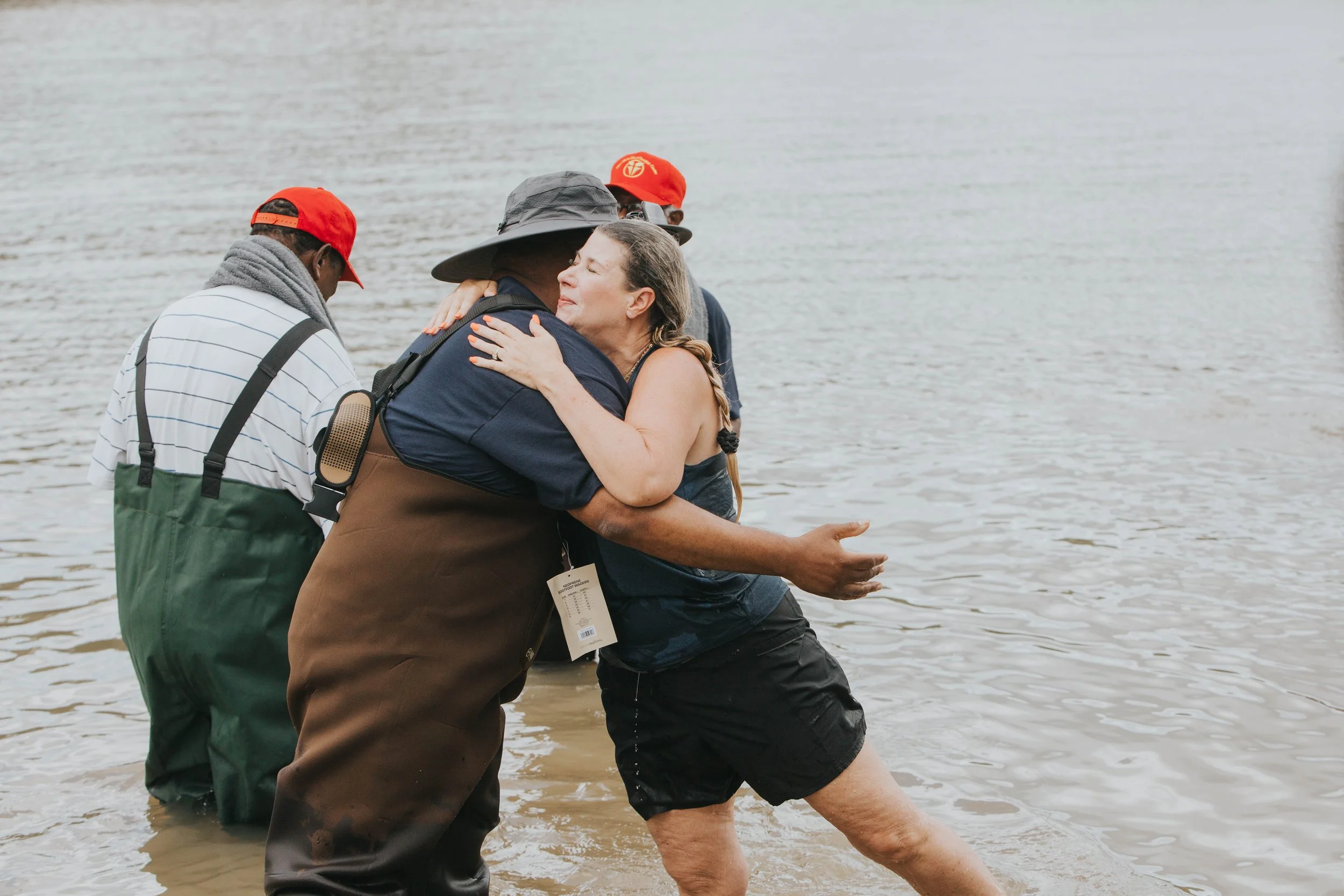 A group of people standing in the water at a beach, embracing and comforting each other.