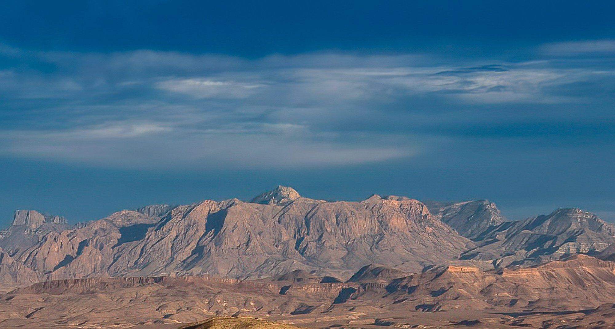 Vast layered mountain range stretching across the West Texas horizon under a soft cloudy sky