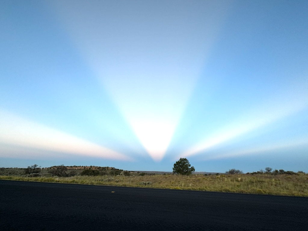 Light rays over road: Dramatic light rays radiating across open sky over empty road and grassland.