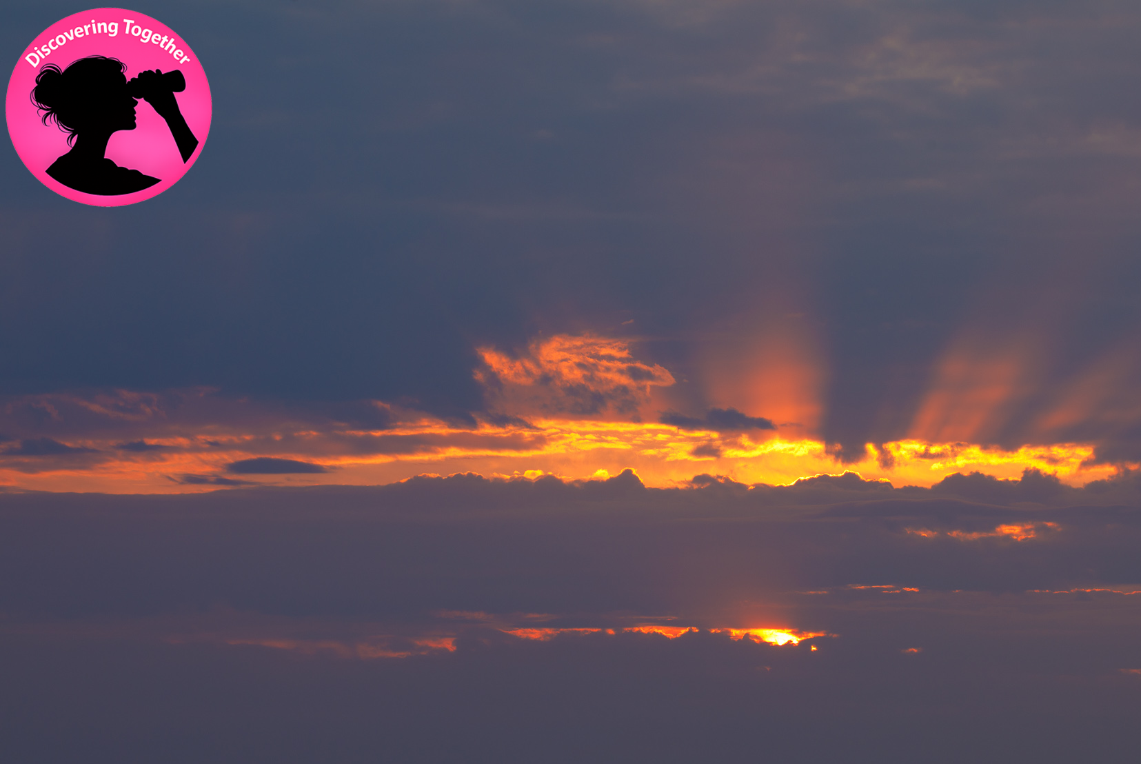 Fiery light rays bursting through storm clouds at sunset over a dark mountain silhouette.