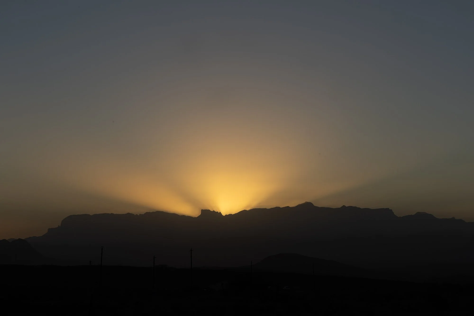 Sun rays fanning over the Chisos Mountain silhouette moments before sunrise in Terlingua, West Texas